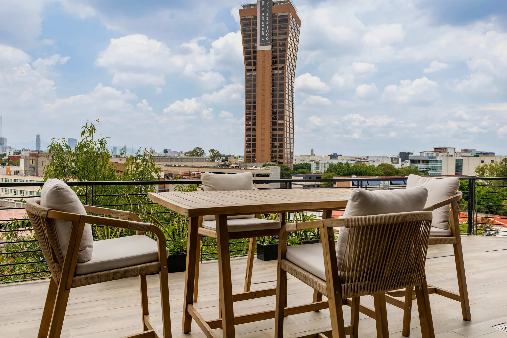 A high-rise building looms over a modern patio with a wooden table and chairs.