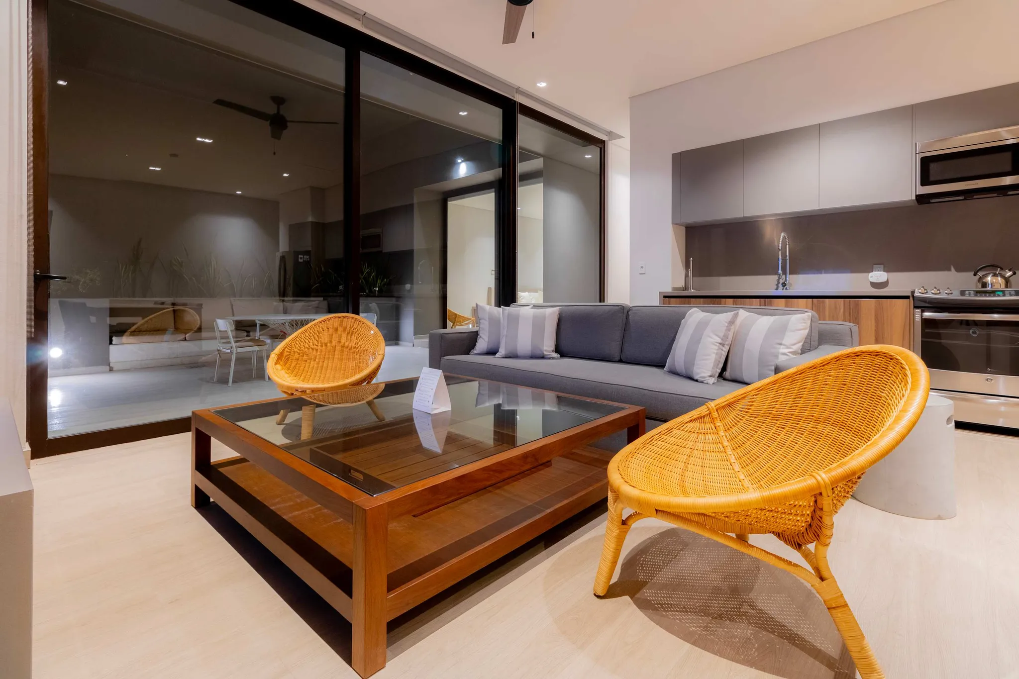 Living room with sofa, coffee table, and chairs, adjacent to a kitchen.