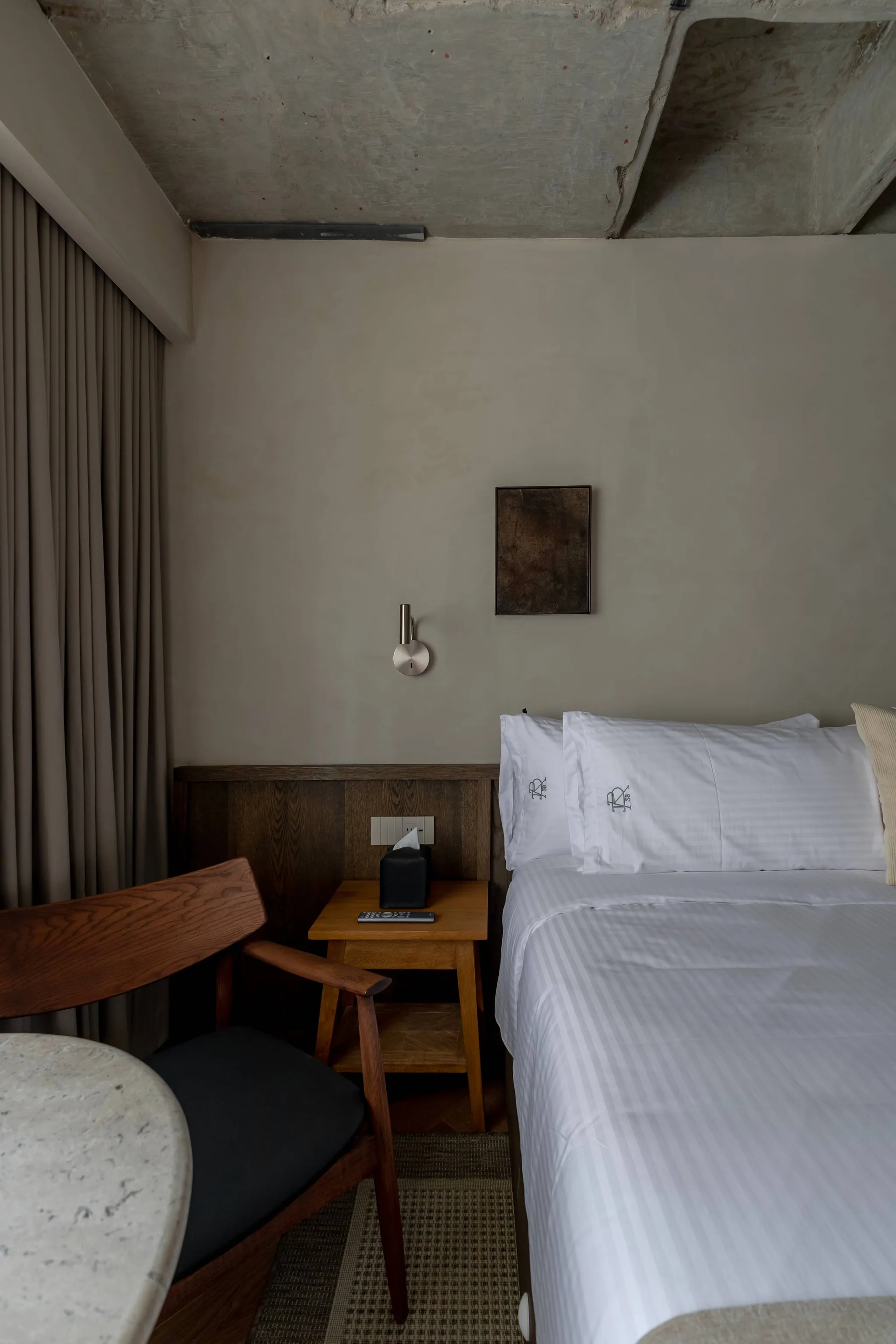 A hotel room with a bed, bedside table, chair, and curtains.