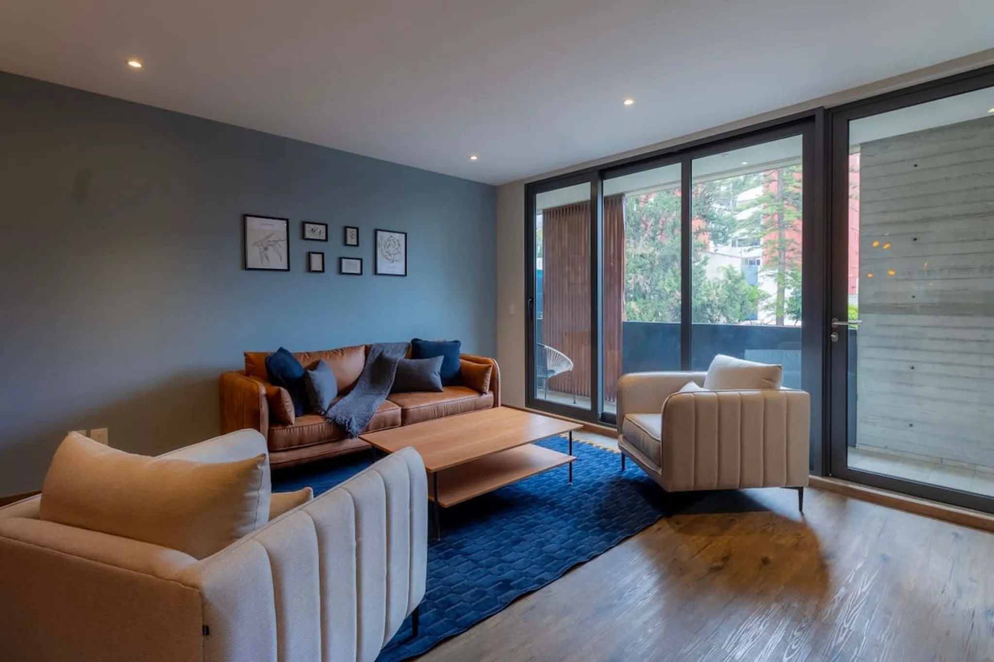 A living room with a brown leather sofa and two cream armchairs.