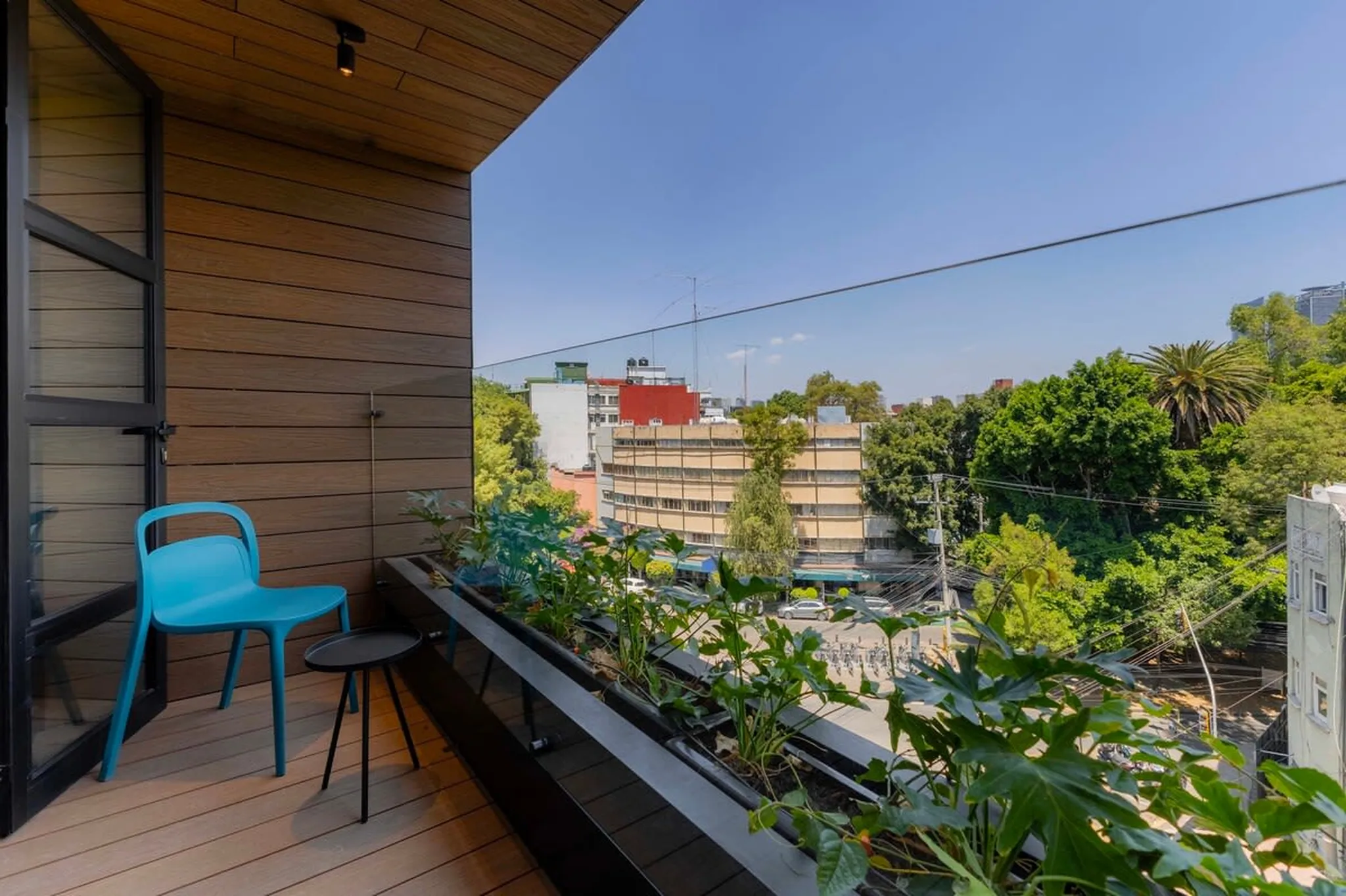 A balcony with a blue chair, small table, and plants overlooking a city street.