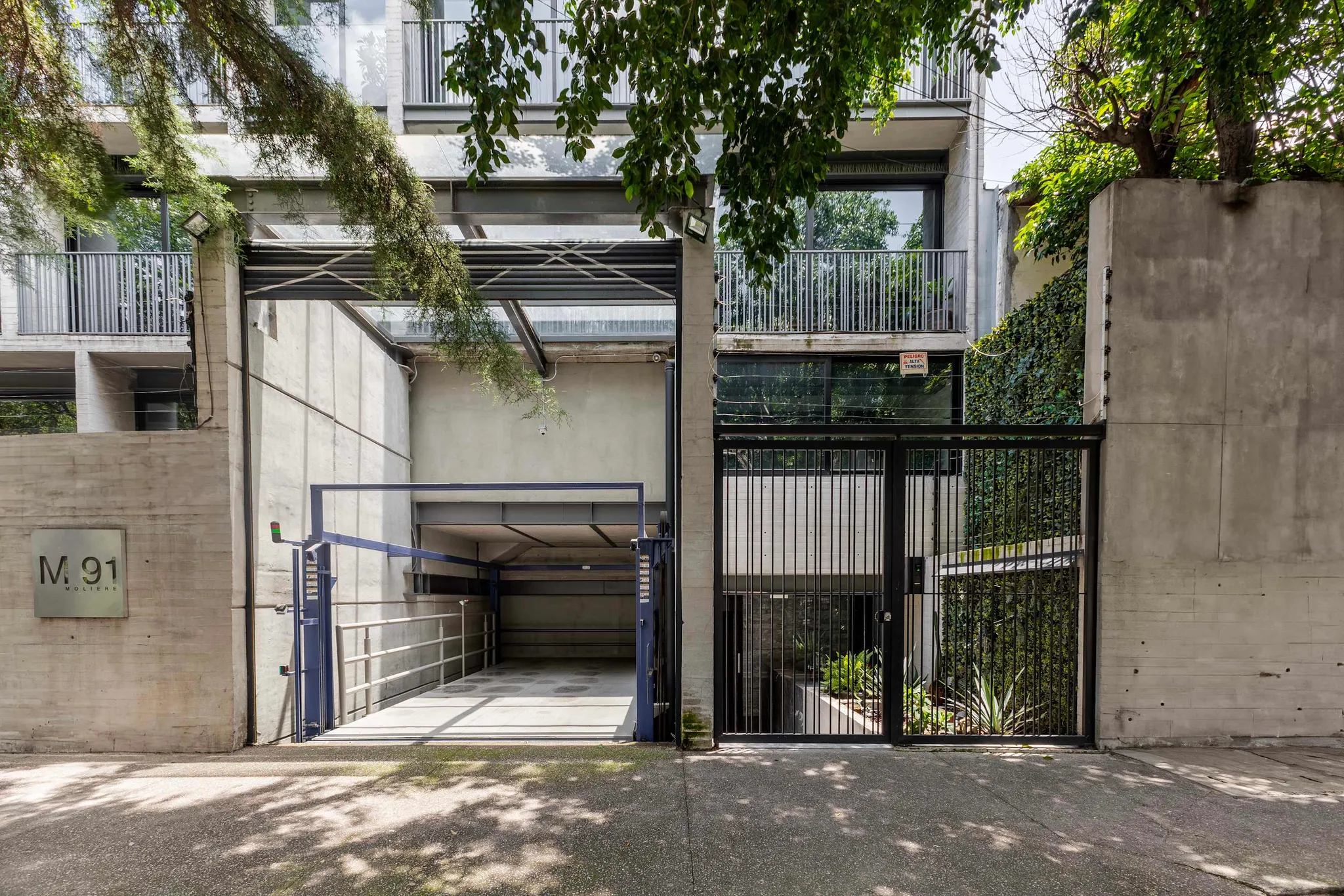 A modern building with a concrete facade, metal balconies, and a garage entrance.