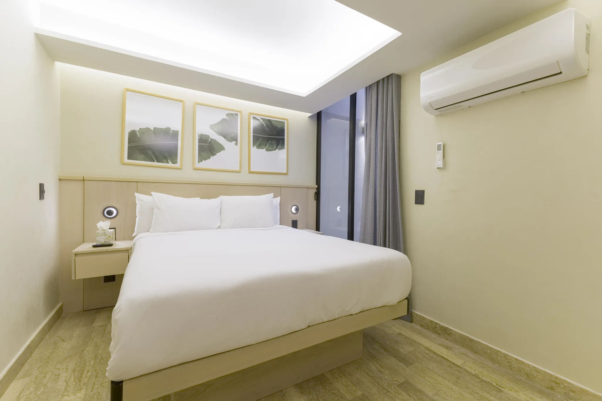 A contemporary bedroom features a king-size bed with white linens, a wooden headboard, and three fra