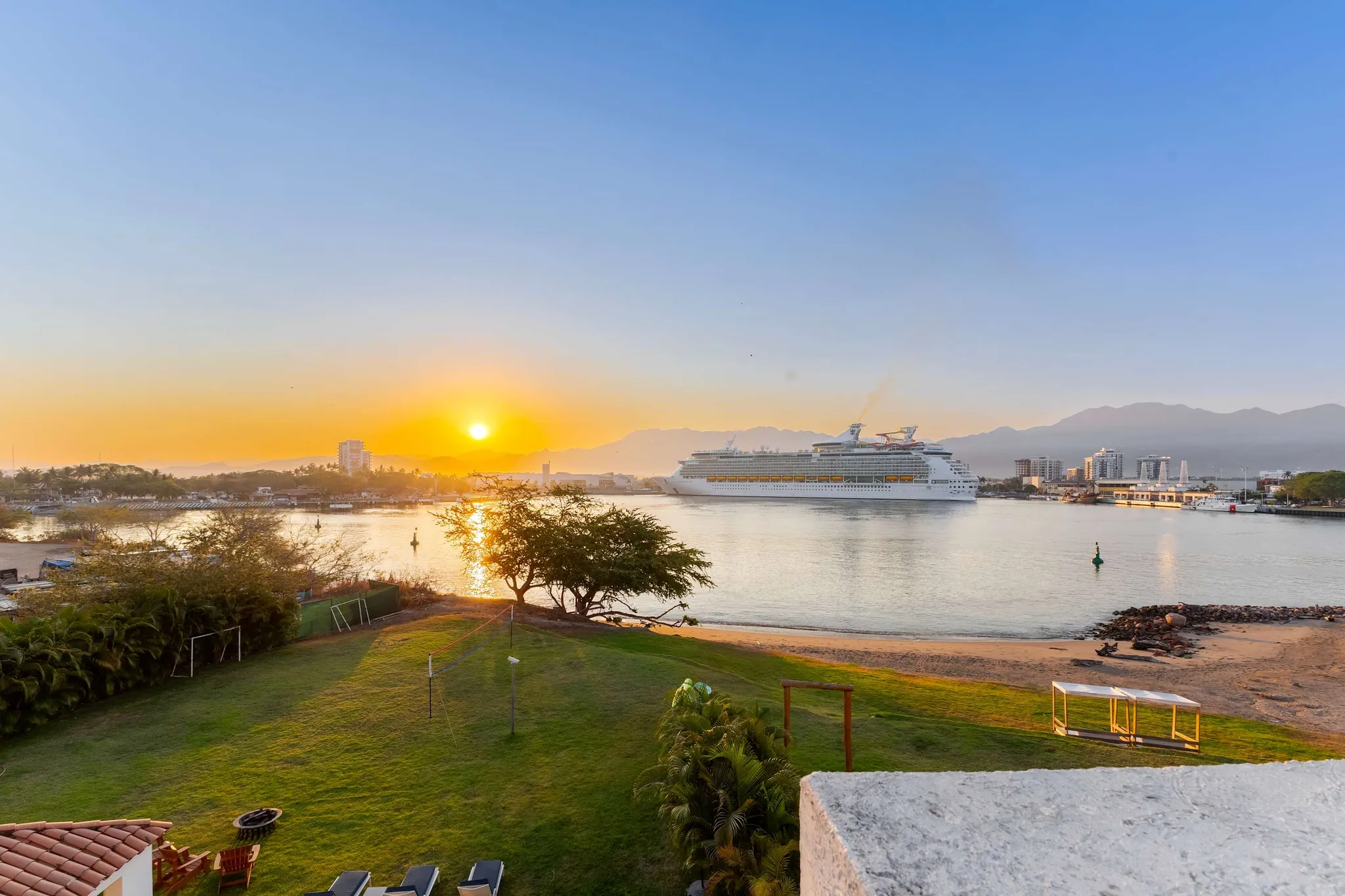 Sunrise over a bay with a cruise ship and distant mountains.