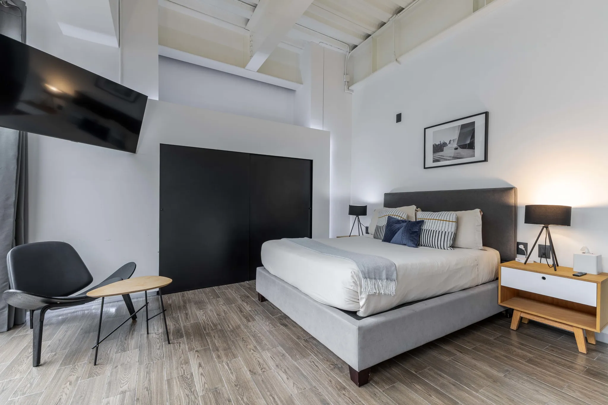 A bedroom with a bed, chair, and TV on a white wall.