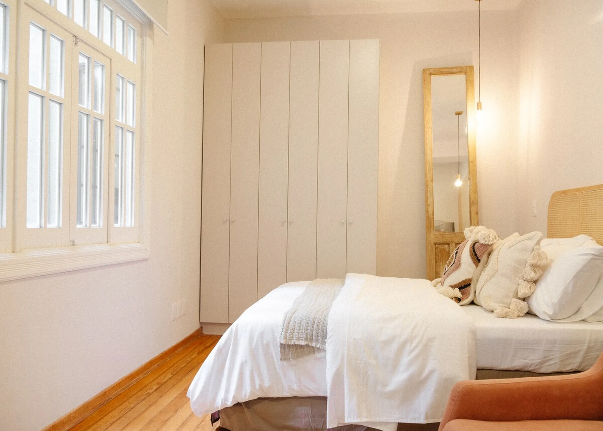 A minimalist bedroom with a window, closet, bed, and mirror.