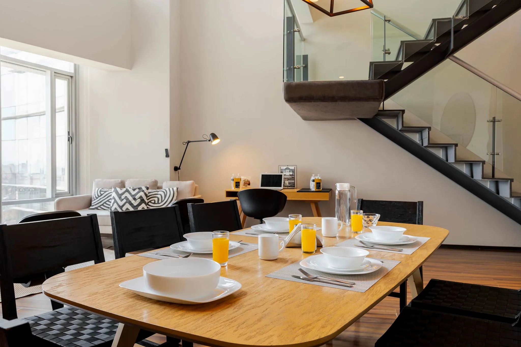 A modern dining room with a wooden table set for a meal, a sofa, and a contemporary staircase.