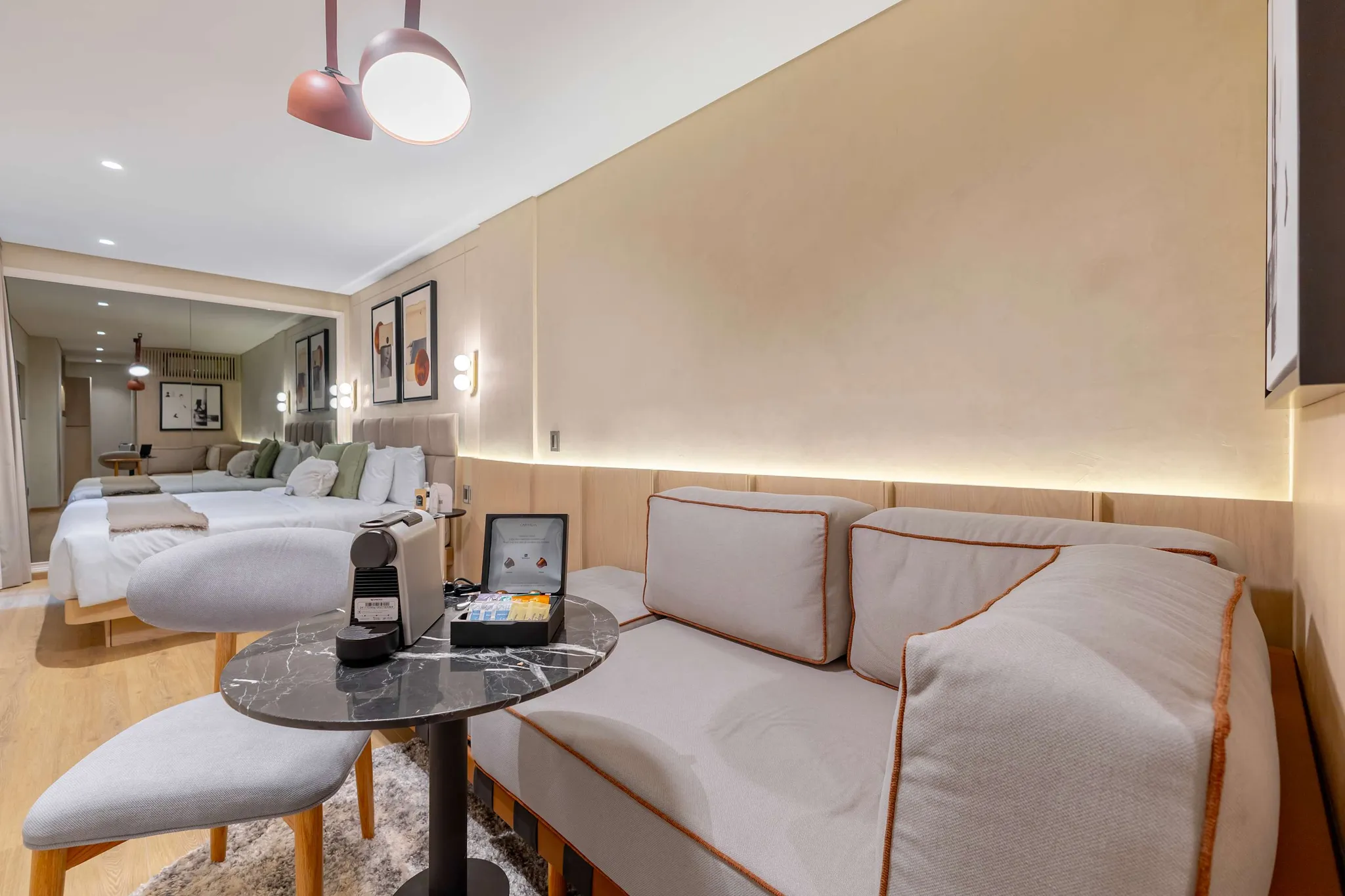 A modern hotel room with a sofa, two beds, and a coffee machine.