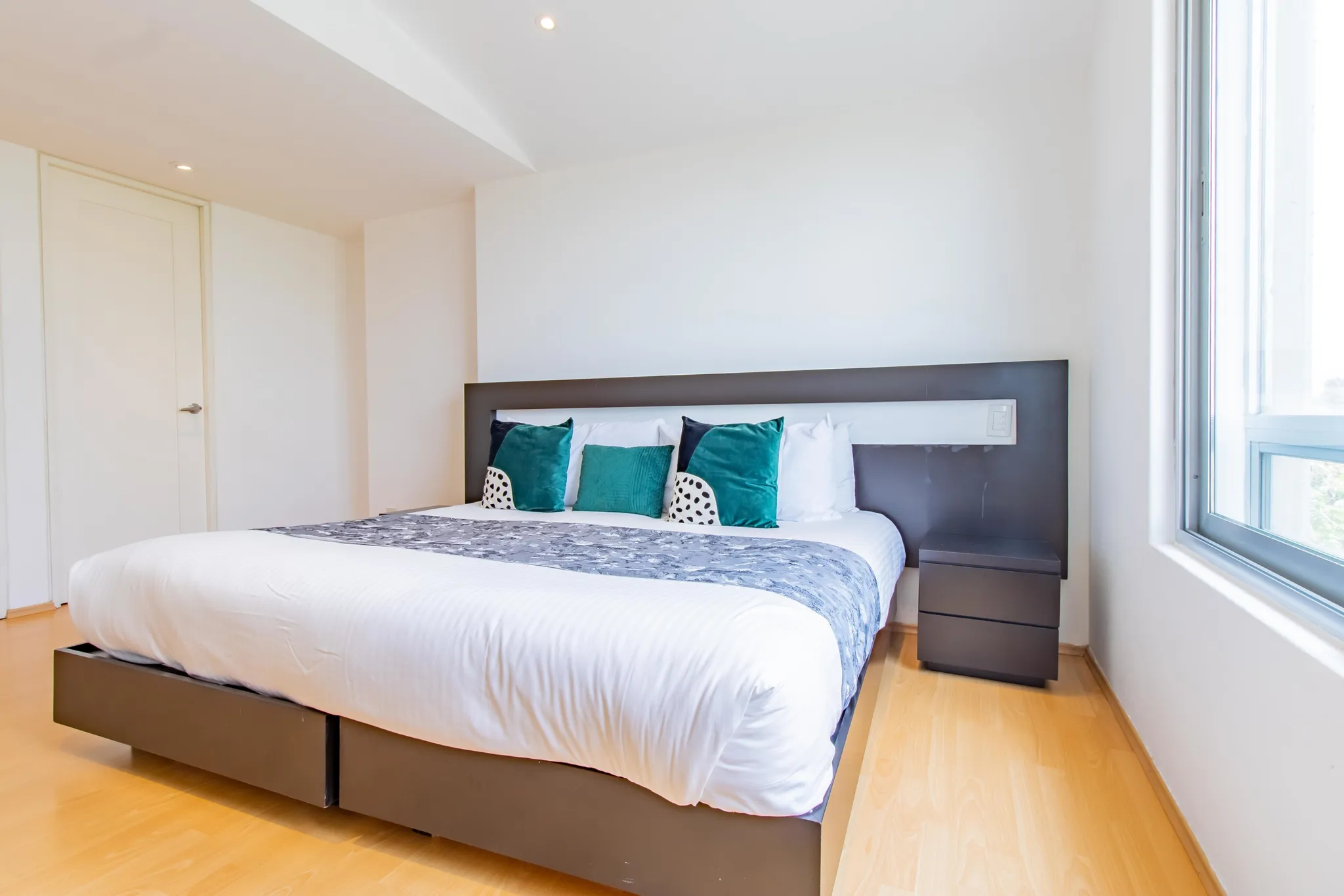 A modern bedroom with a large bed and teal pillows.
