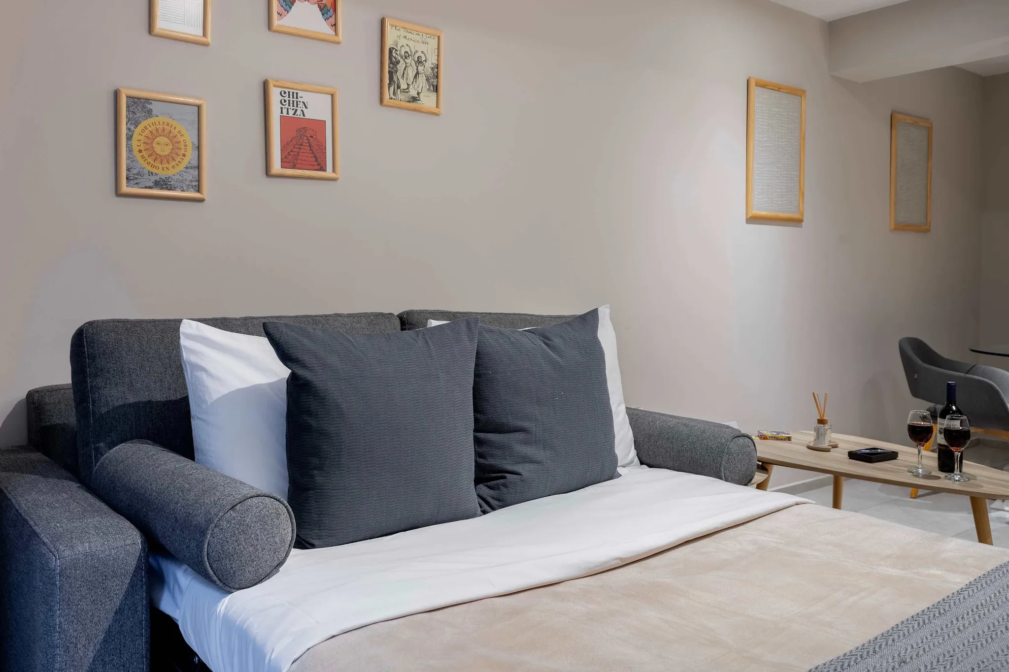 A sofa with a white sheet and gray pillows with a wooden coffee table and wine glasses.