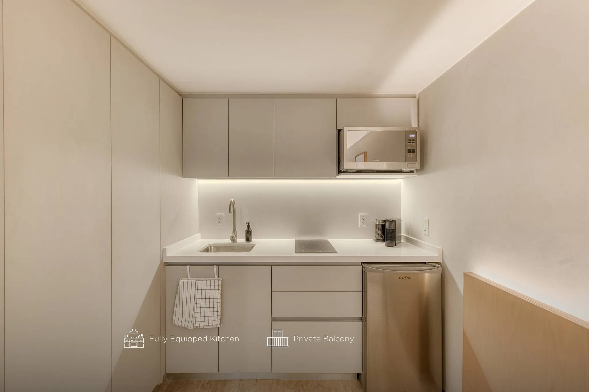 A modern, minimalist kitchen with light-colored cabinets, a microwave, and a small refrigerator.