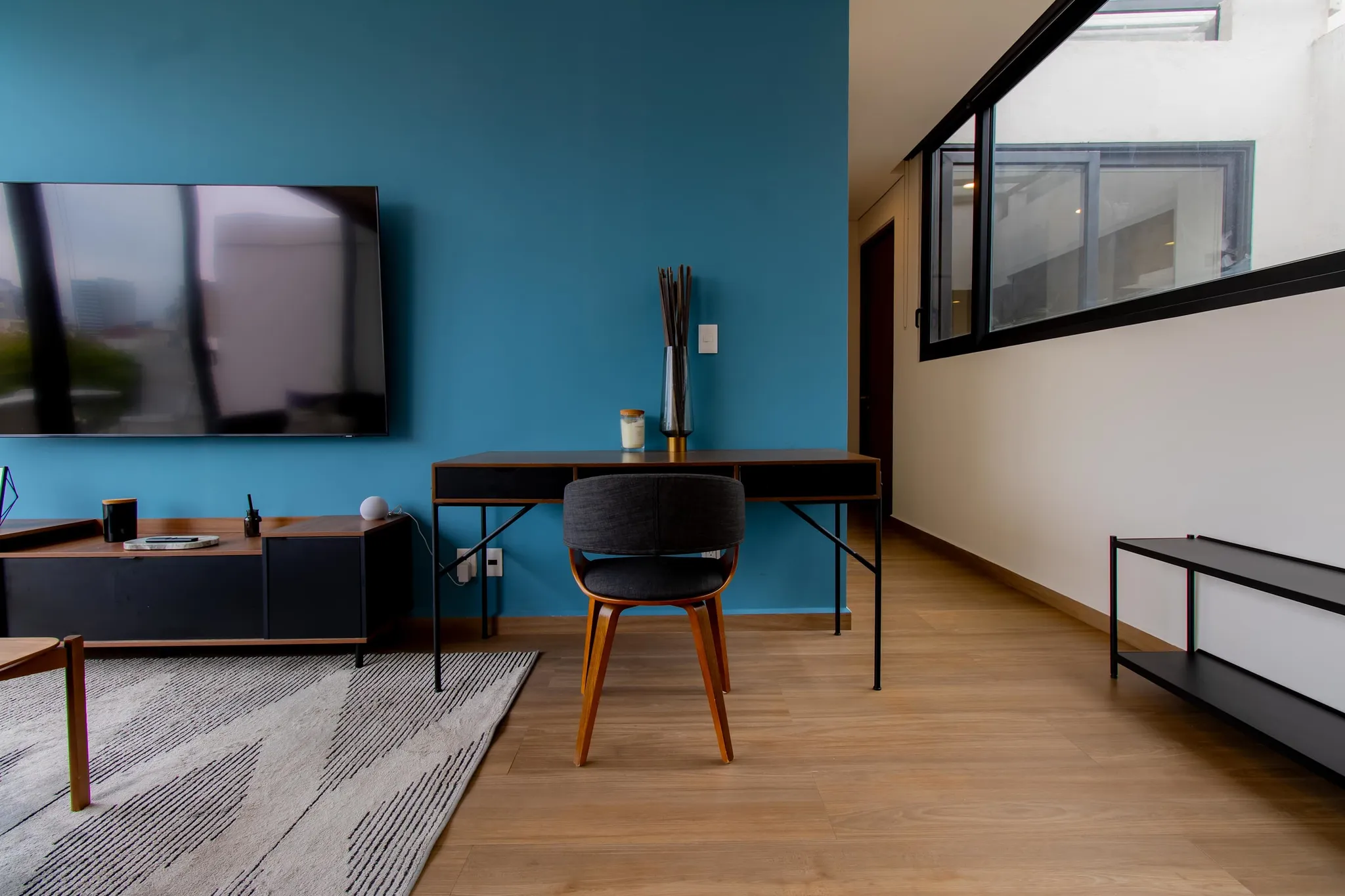 A black desk and chair against a deep blue wall with a mounted TV at Downtown del Valle.
