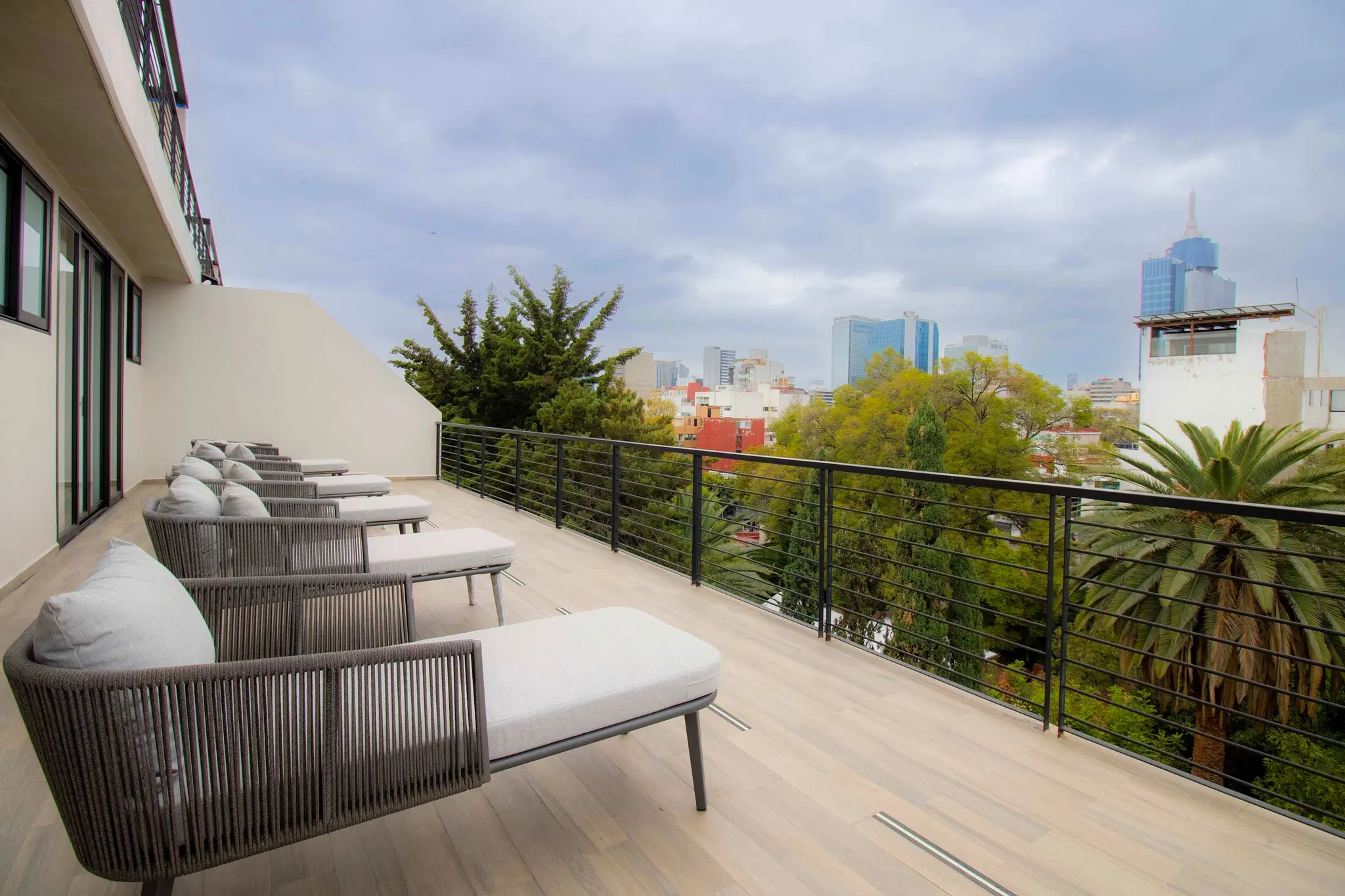 Modern balcony with lounge chairs, overlooking a cityscape with trees and buildings.
