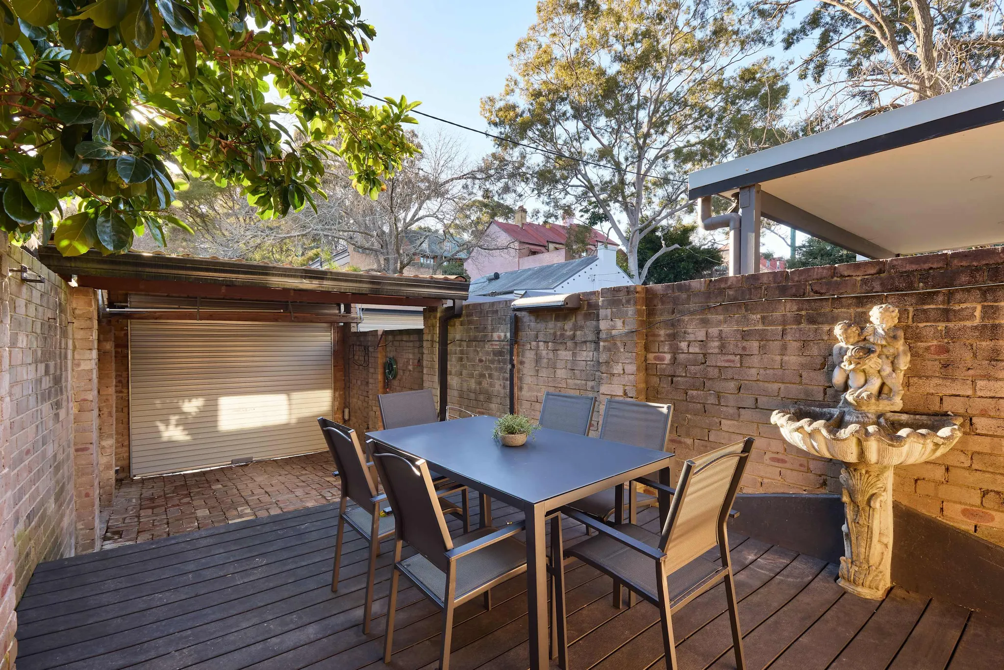 Backyard deck with a dining table and chairs against a brick wall with a fountain at the Glebe house