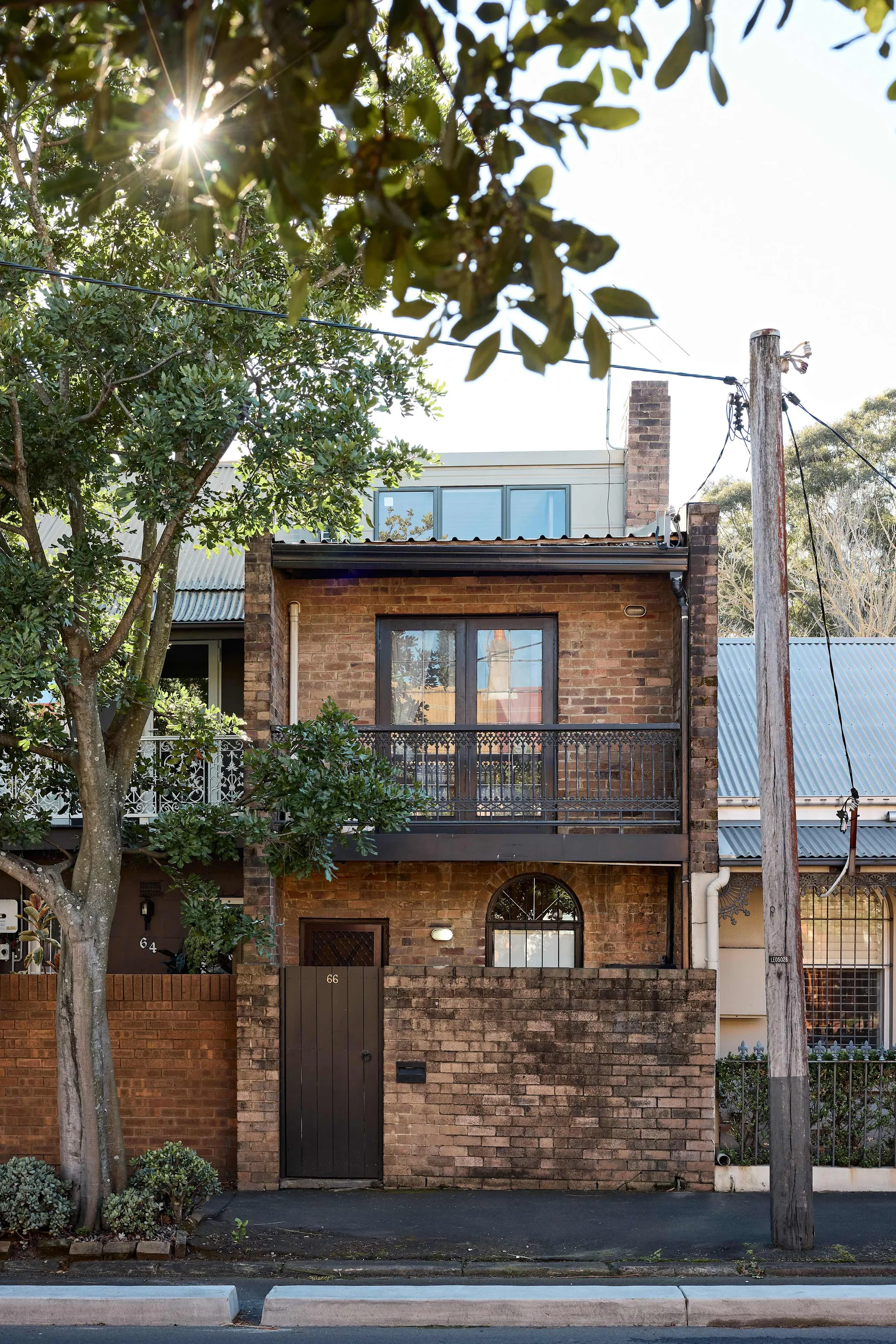 Brick Glebe townhouse with a first-floor iron balcony framed by trees