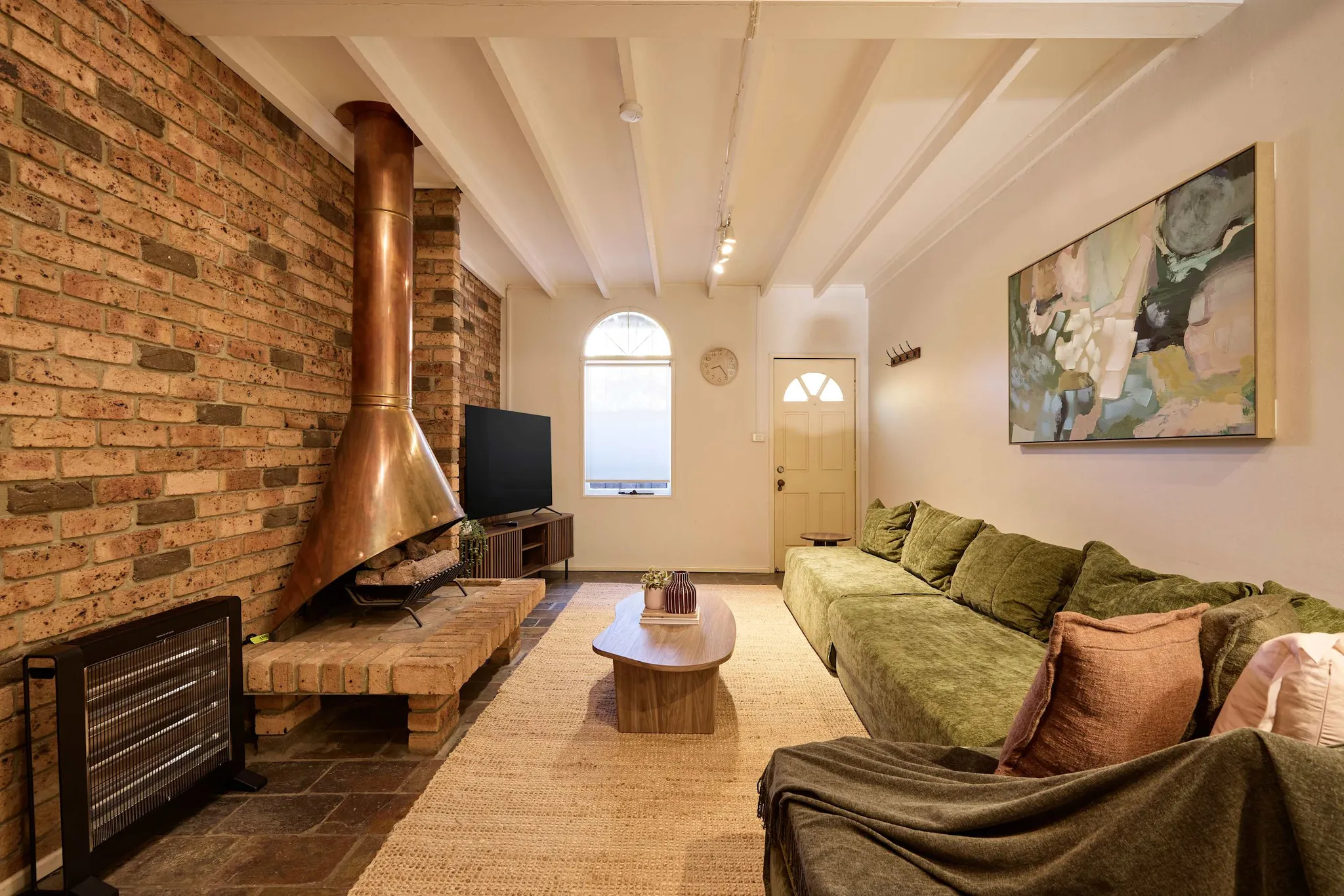 Living room with an exposed brick wall, copper fireplace, green velvet sofa and timber coffee table in the Glebe house