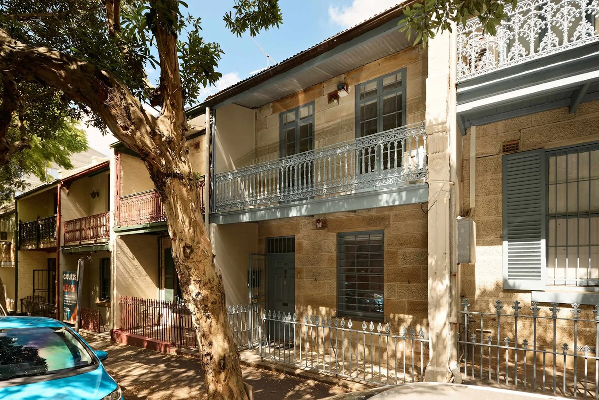 Row of historic Surry Hills terrace houses with ornate iron-lace balconies and a street tree, home to the 4BR house