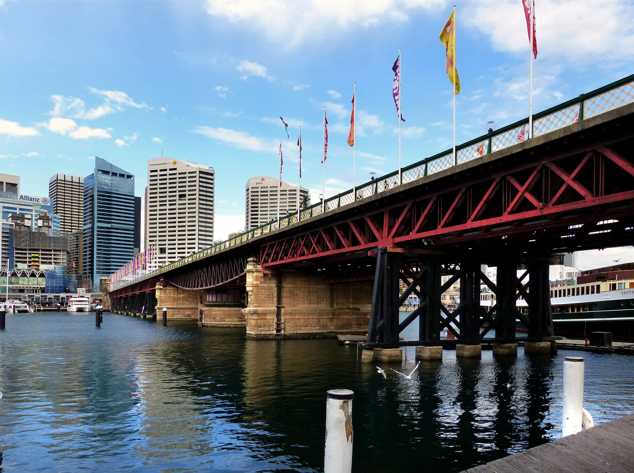 Pyrmont Bridge over Darling Harbour with flags flying and the Sydney CBD towers behind