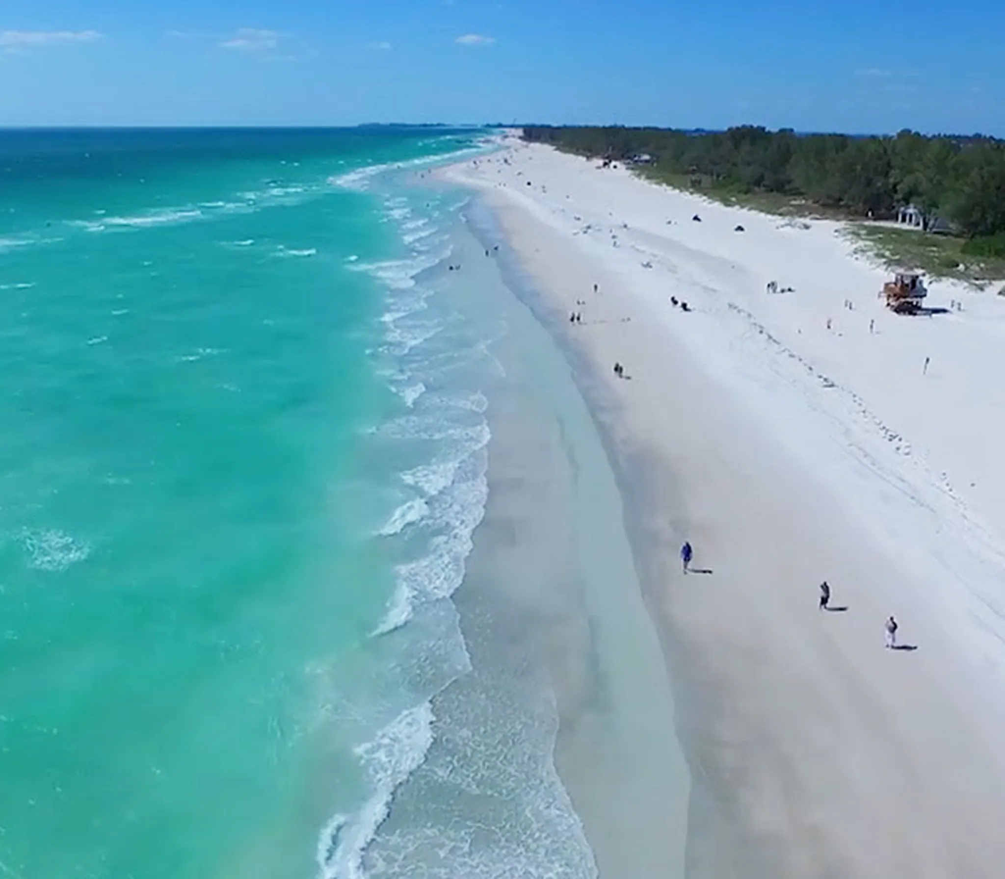 Sun hat and flip-flops on white sand beach with turquoise ocean waves in the background