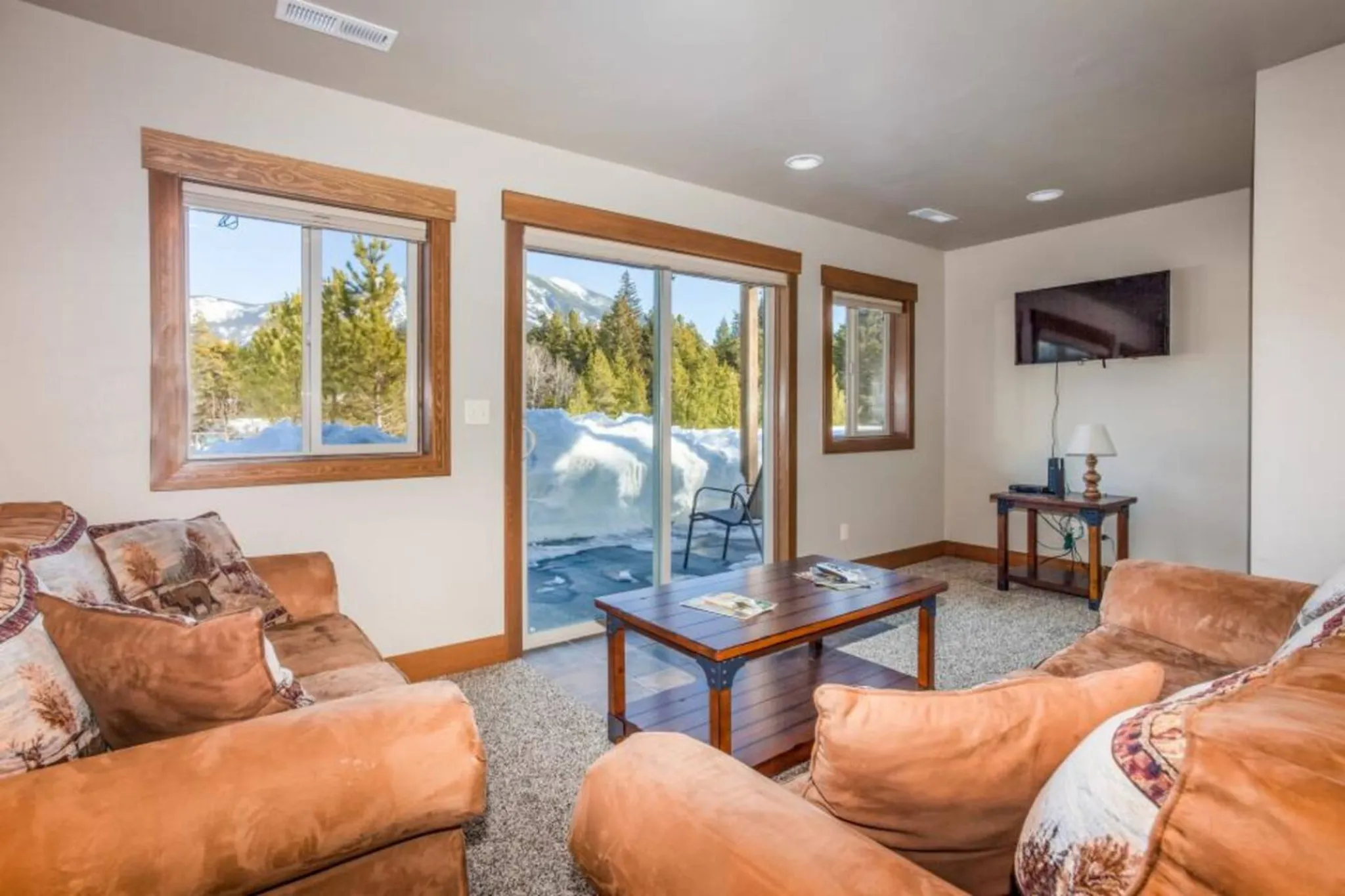 Living room with plush orange sofas, a coffee table, and a sliding glass door opening to a snowy mou