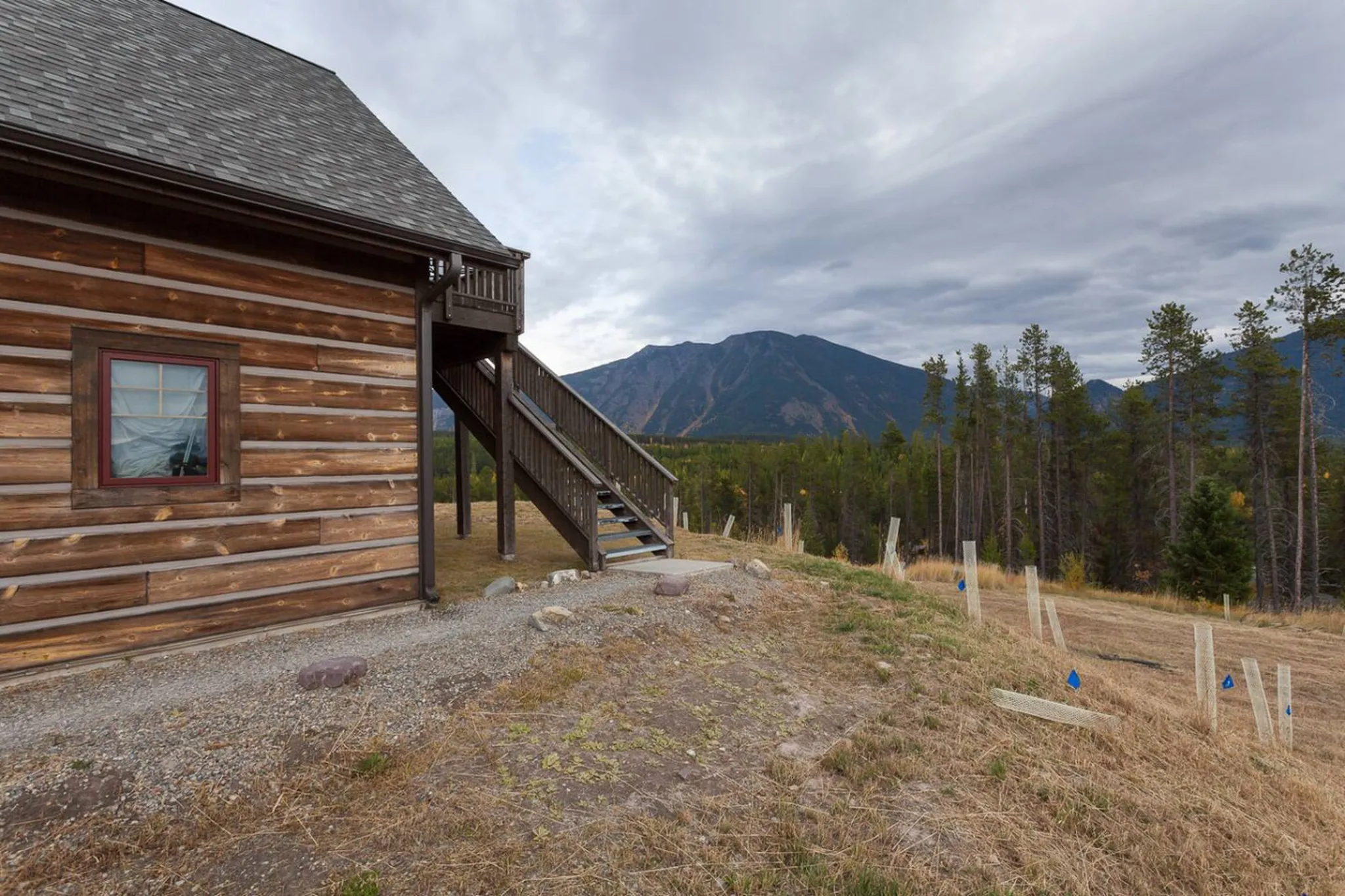 Log cabin with wooden stairs leading up to a deck, with a mountain and forest in the background.