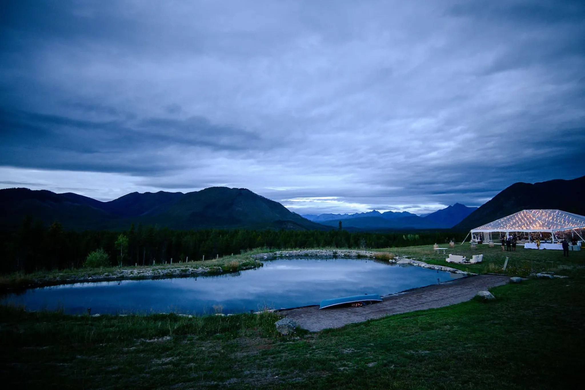 A vast mountainous landscape under a stormy sky with a tent and pond.