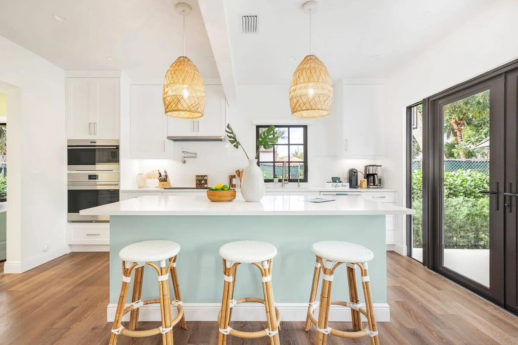 Kitchen with a light blue island, white counters and rattan pendant lights in a Hotel Home Stays home