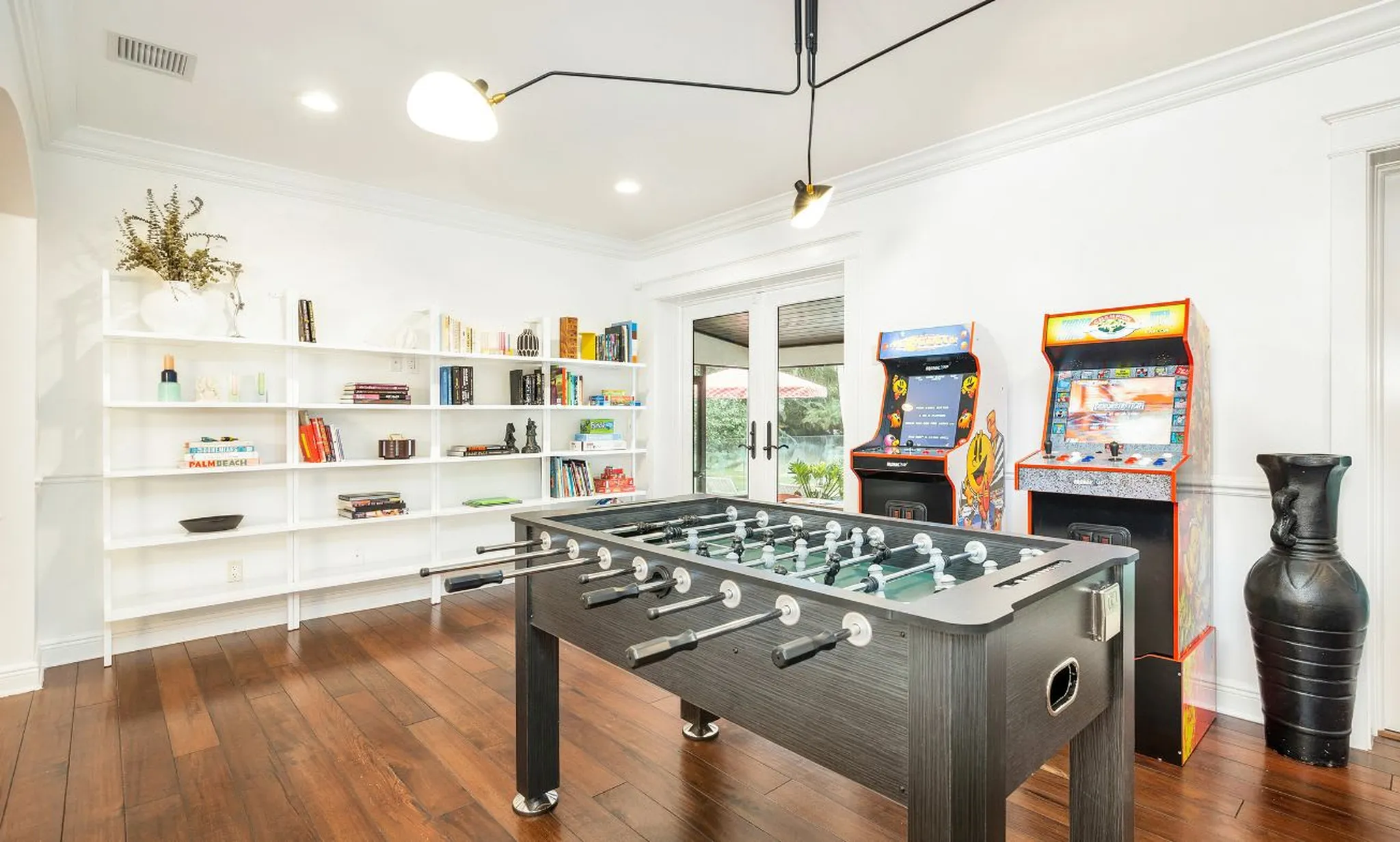 Game room with a foosball table, two arcade machines, and shelves of board games