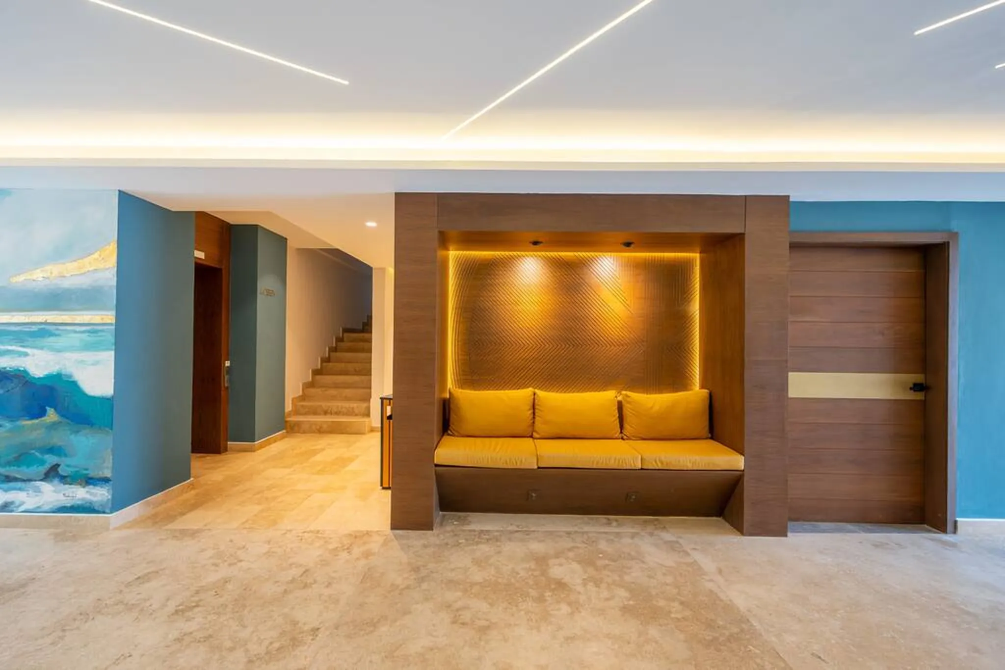 Kippal lobby with a lit wood niche and mustard-yellow bench, a sea mural on a teal wall and stairs leading up