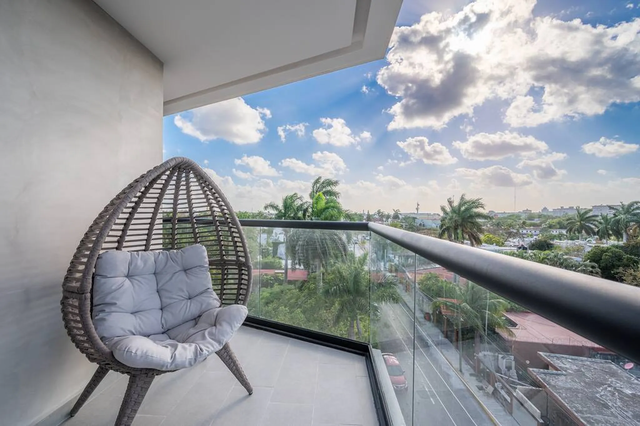 Egg-shaped wicker chair on a balcony overlooking palm trees and rooftops