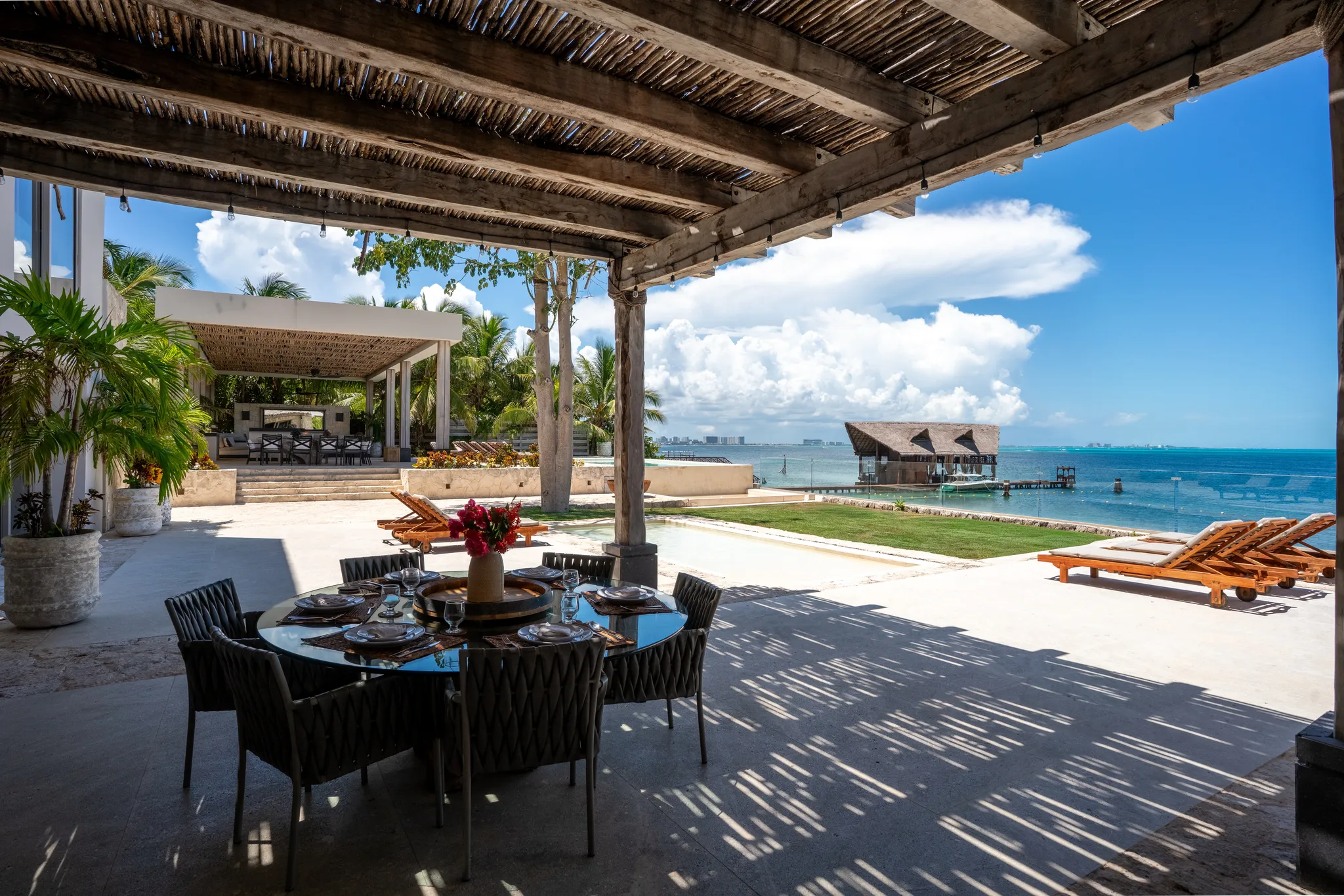 Luxury beachfront villa terrace in Cancún set up for a corporate retreat, featuring outdoor dining, ocean views, lounge chairs and spacious gathering areas by the water