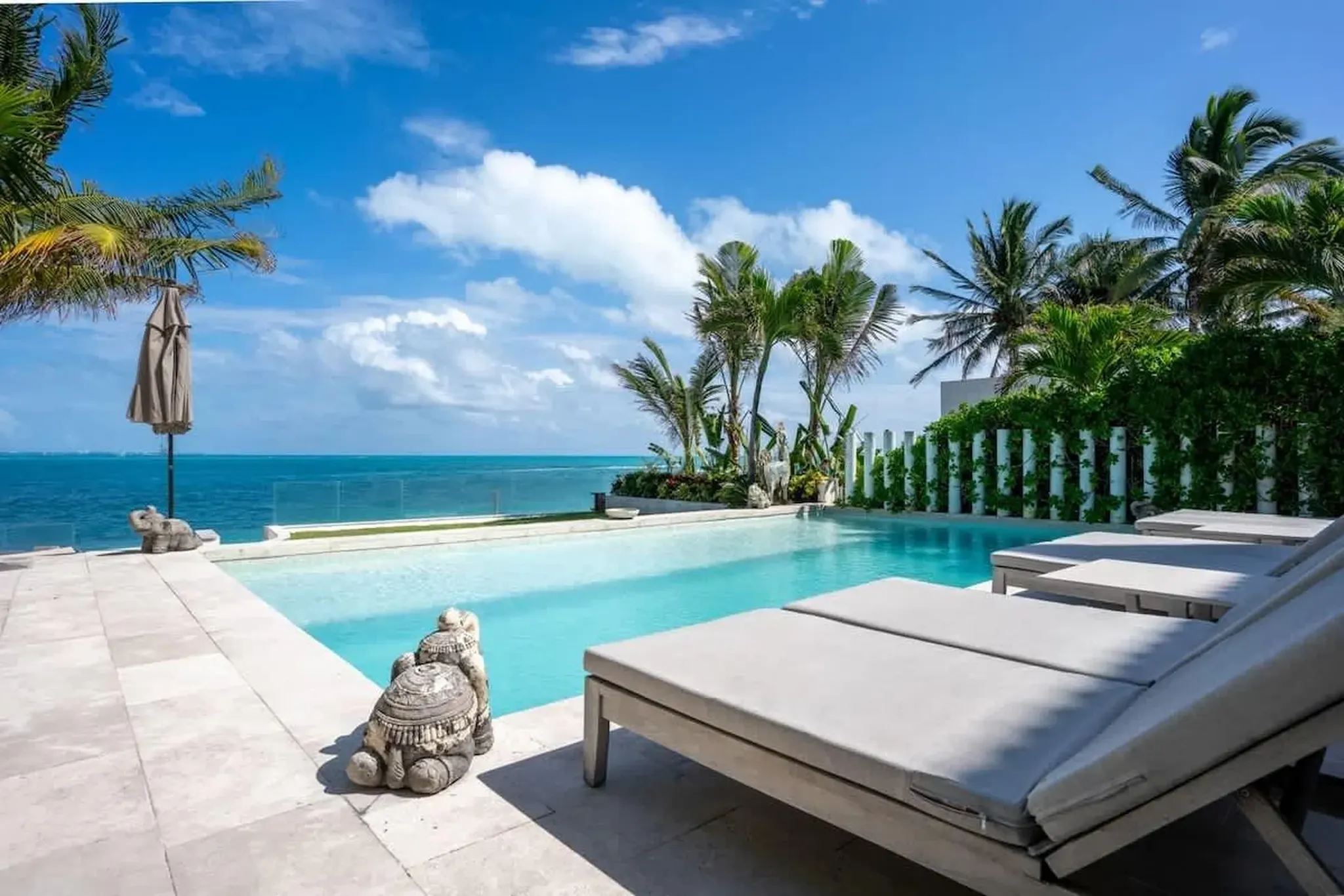 Luxury oceanfront villa pool with lounge chairs, tropical palm trees, and panoramic Caribbean Sea views in the Riviera Maya