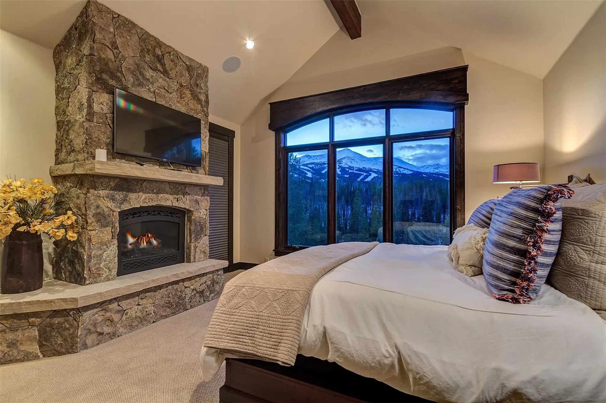 Kitchen with wood cabinets, granite counters, stainless steel appliances, and pendant lights near a stone fireplace in the living area