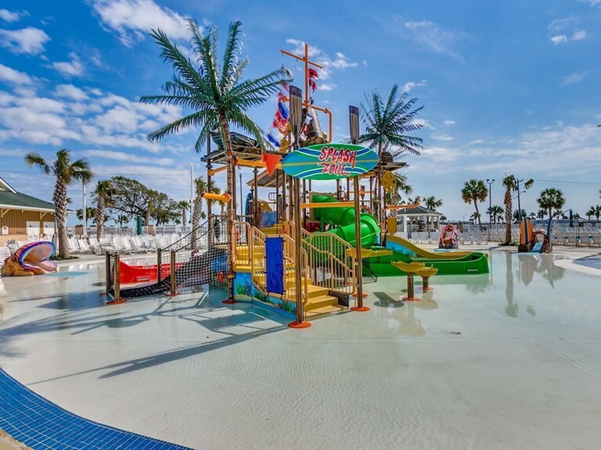 Colorful waterpark with slides, mushroom-shaped feature, and palm trees reflecting in pool.
