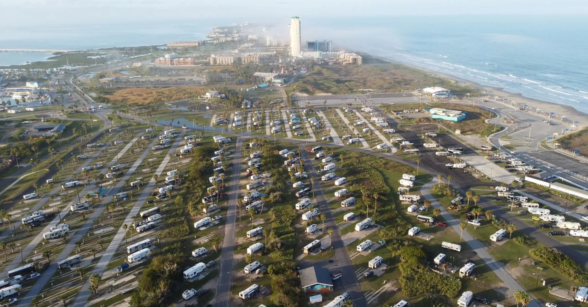 Aerial view of a coastal RV park near the ocean, showcasing numerous caravans and nearby resort buildings.