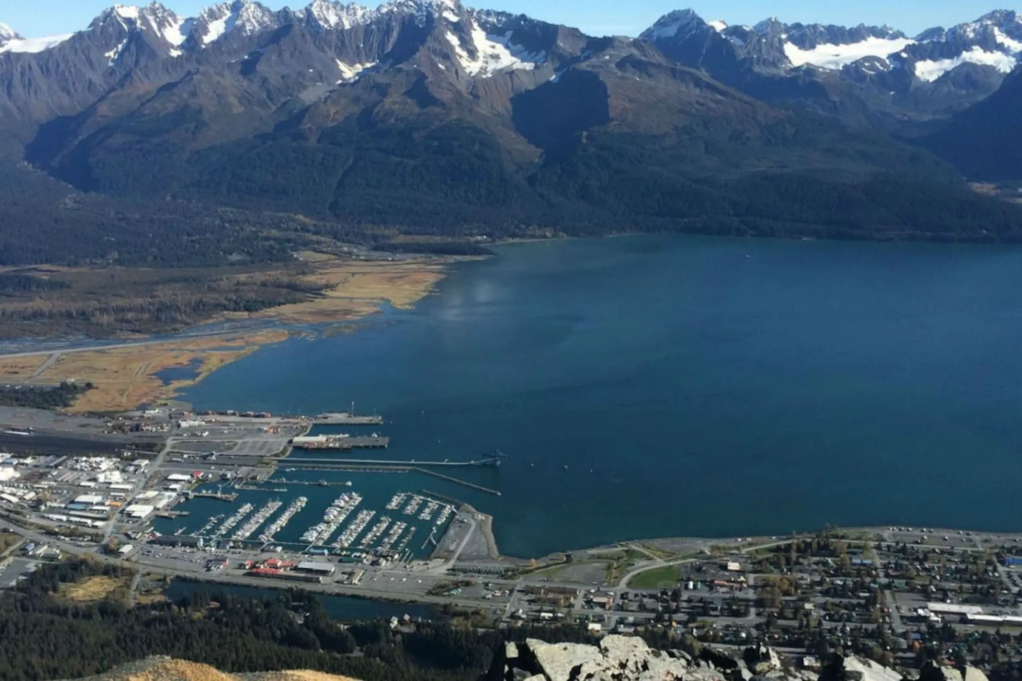 Aerial view of a coastal town with a harbor, surrounded by mountains and a large body of water.