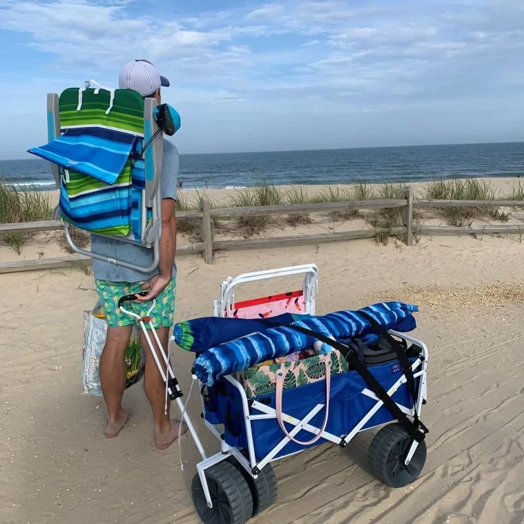Folded beach chairs, a beach umbrella and rolling cart in a corner by a blue wall and white fence