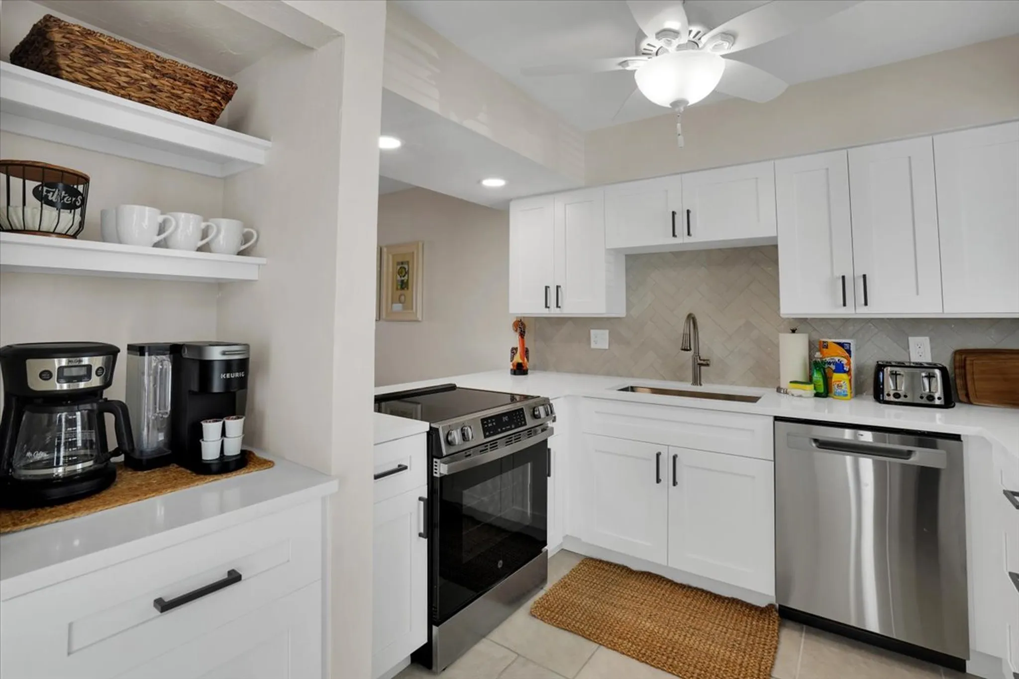 Bright kitchen with white cabinets, stainless steel oven and dishwasher, microwave, coffee makers, and a window above the sink