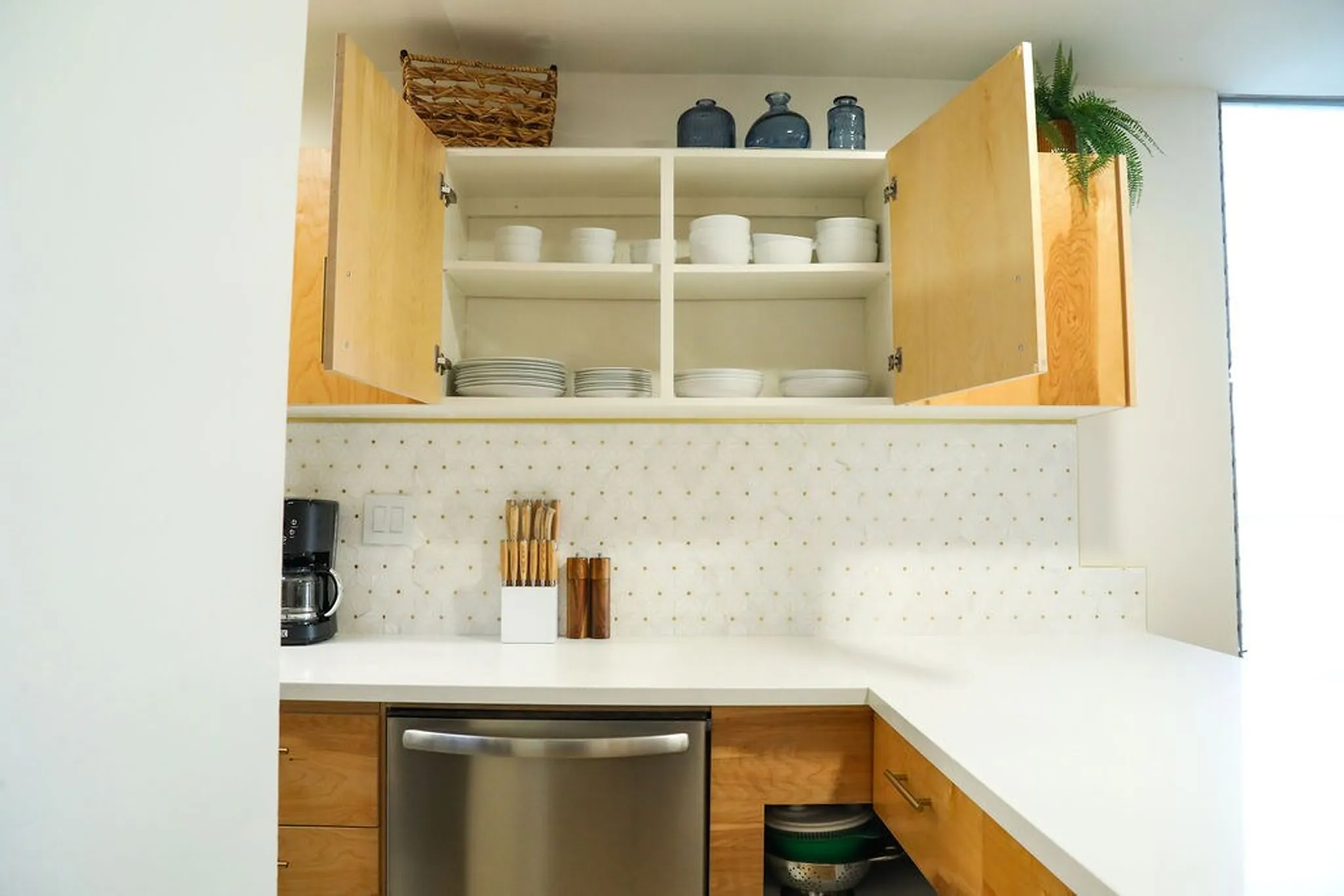 Kitchen cabinets with open doors reveal shelves stocked with dishes, bowls, and decorative jars.