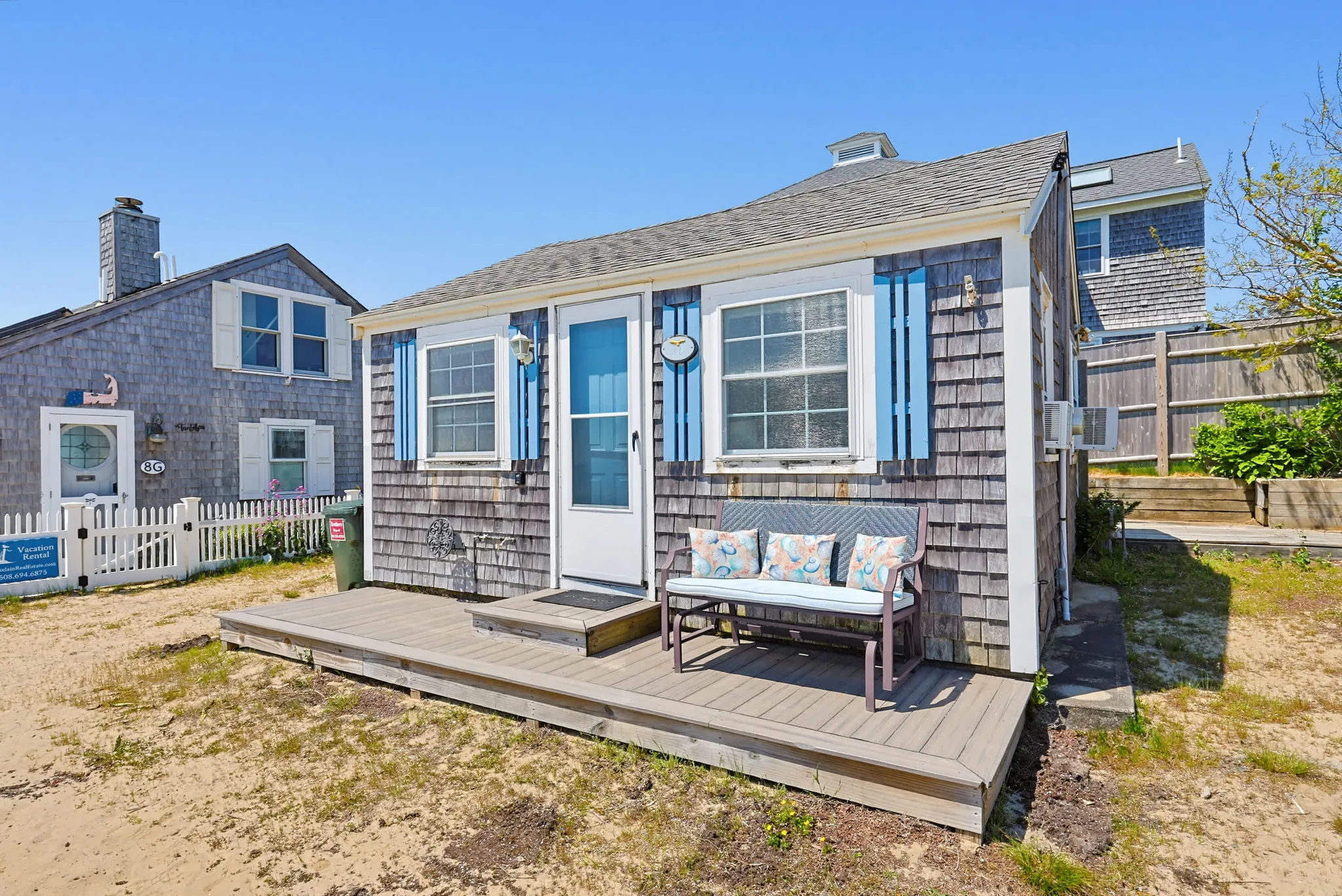 Weathered cedar-shingled Cape Cod beach cottage with blue shutters and a small deck in Dennis