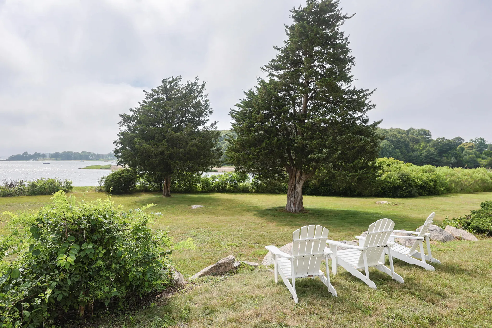 White Adirondack chairs on a lawn overlooking a calm bay in Bourne, Cape Cod