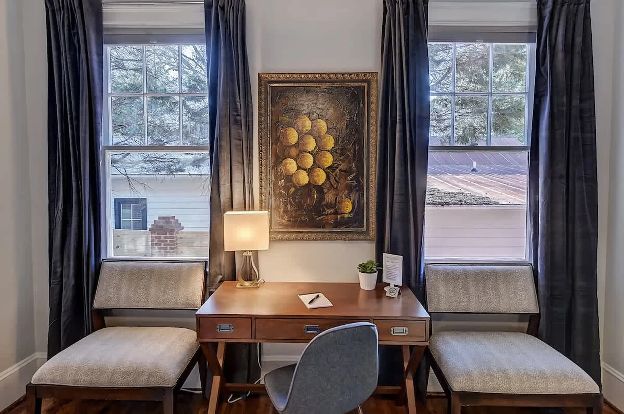 A wooden desk and two upholstered chairs beside a framed painting, a work-from-home nook