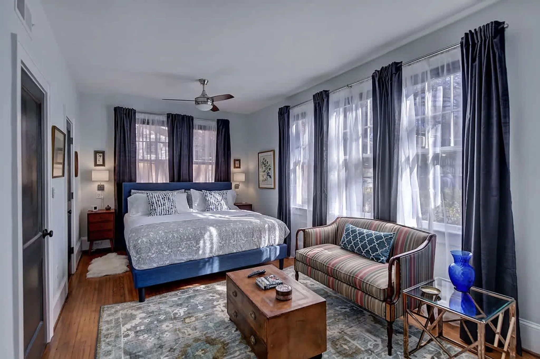 Bedroom with a blue upholstered bed, striped sofa, and a wooden coffee table