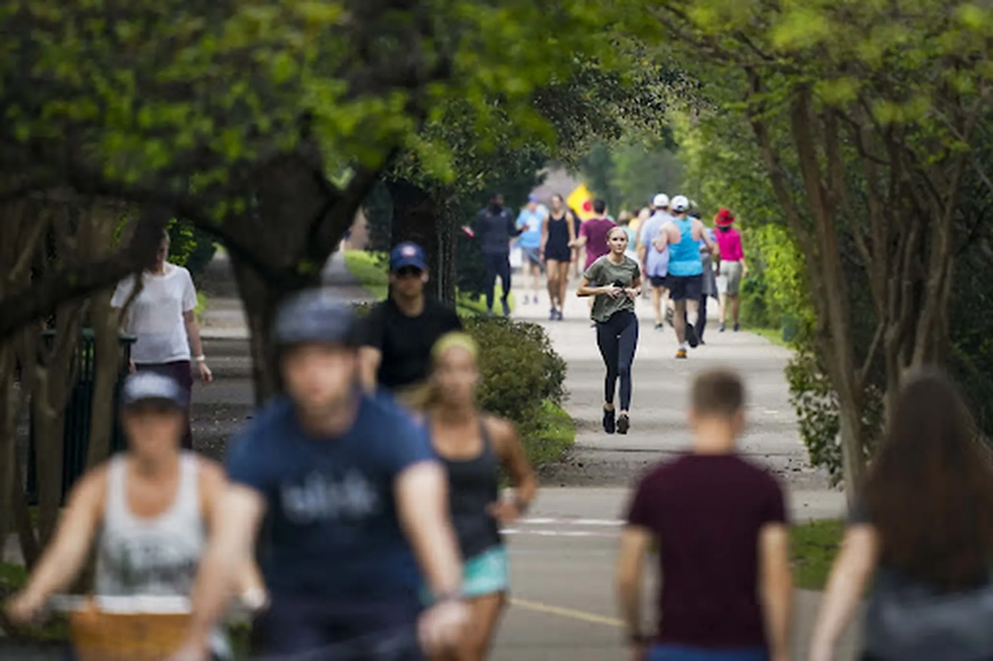 Joggers and cyclists on Katy Trail, with lush greenery and skyline views.