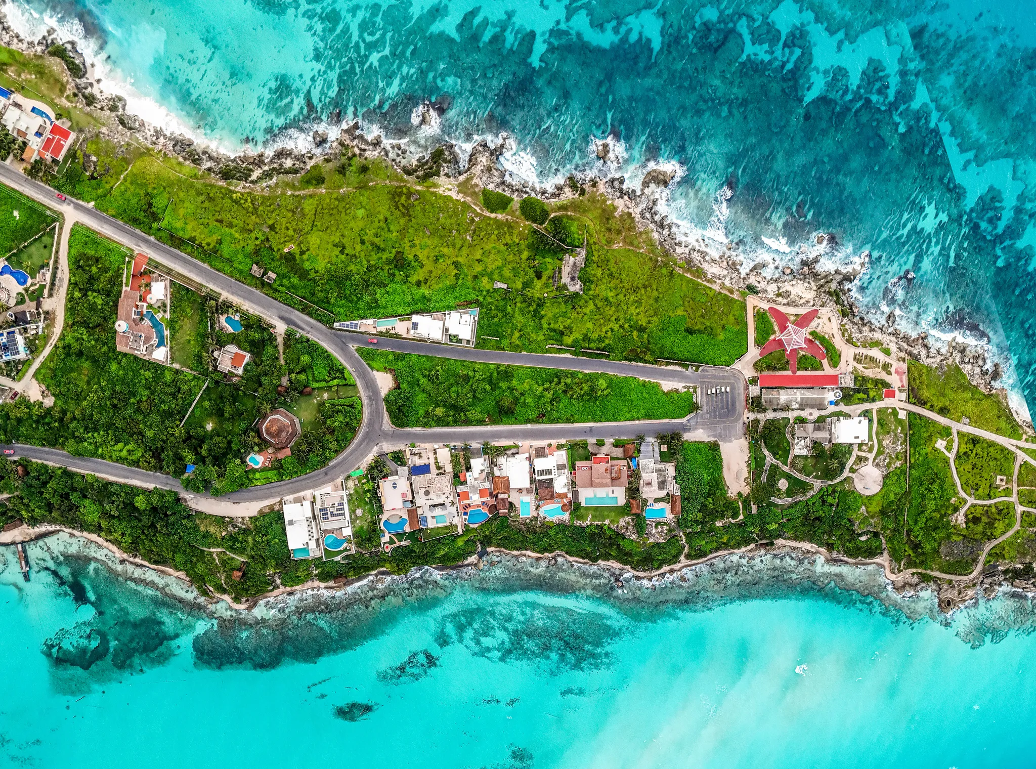 Aerial view of beachfront villas with pools and lush greenery along the shoreline.
