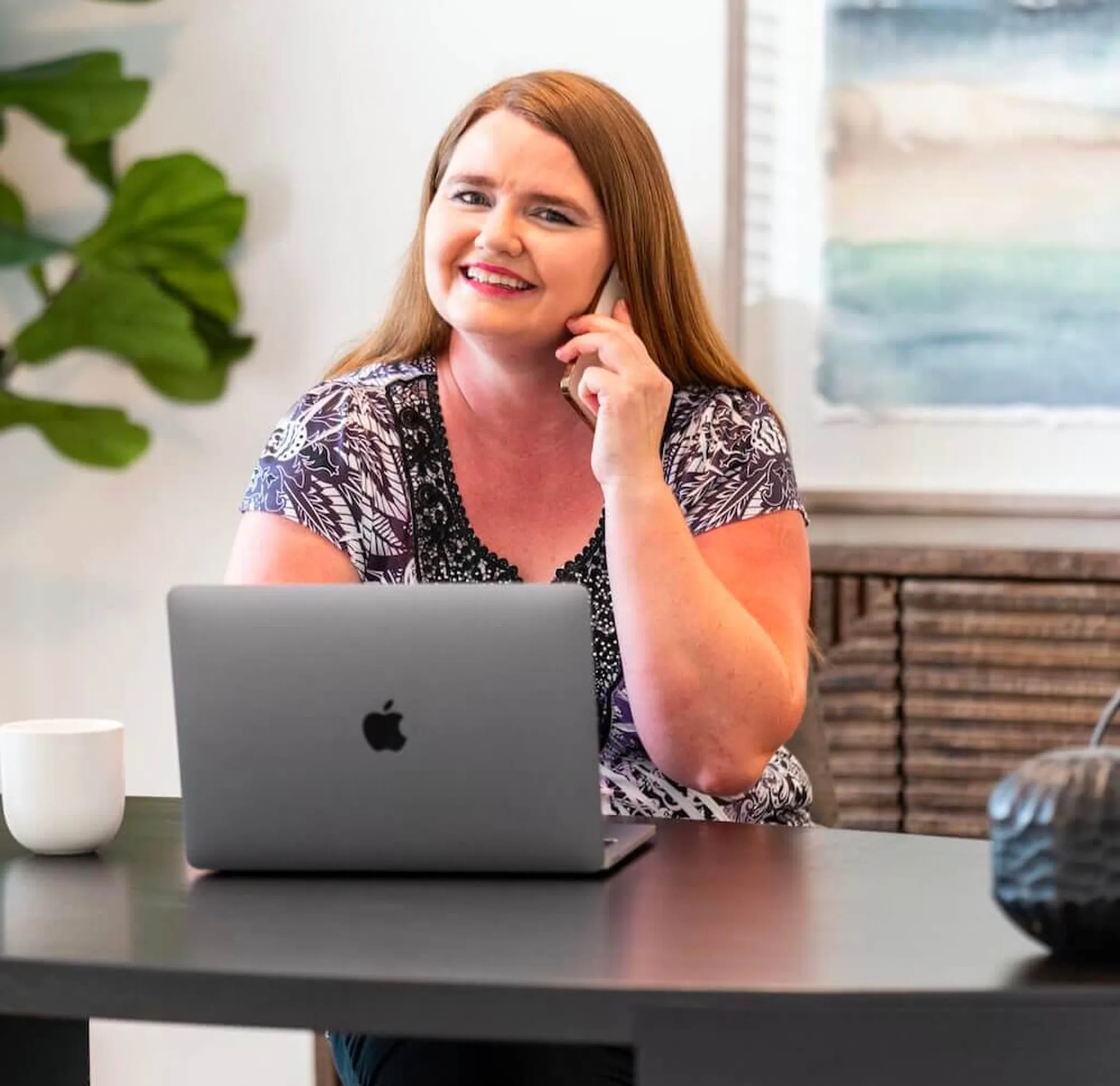 image of woman on phone working on her laptop smiling