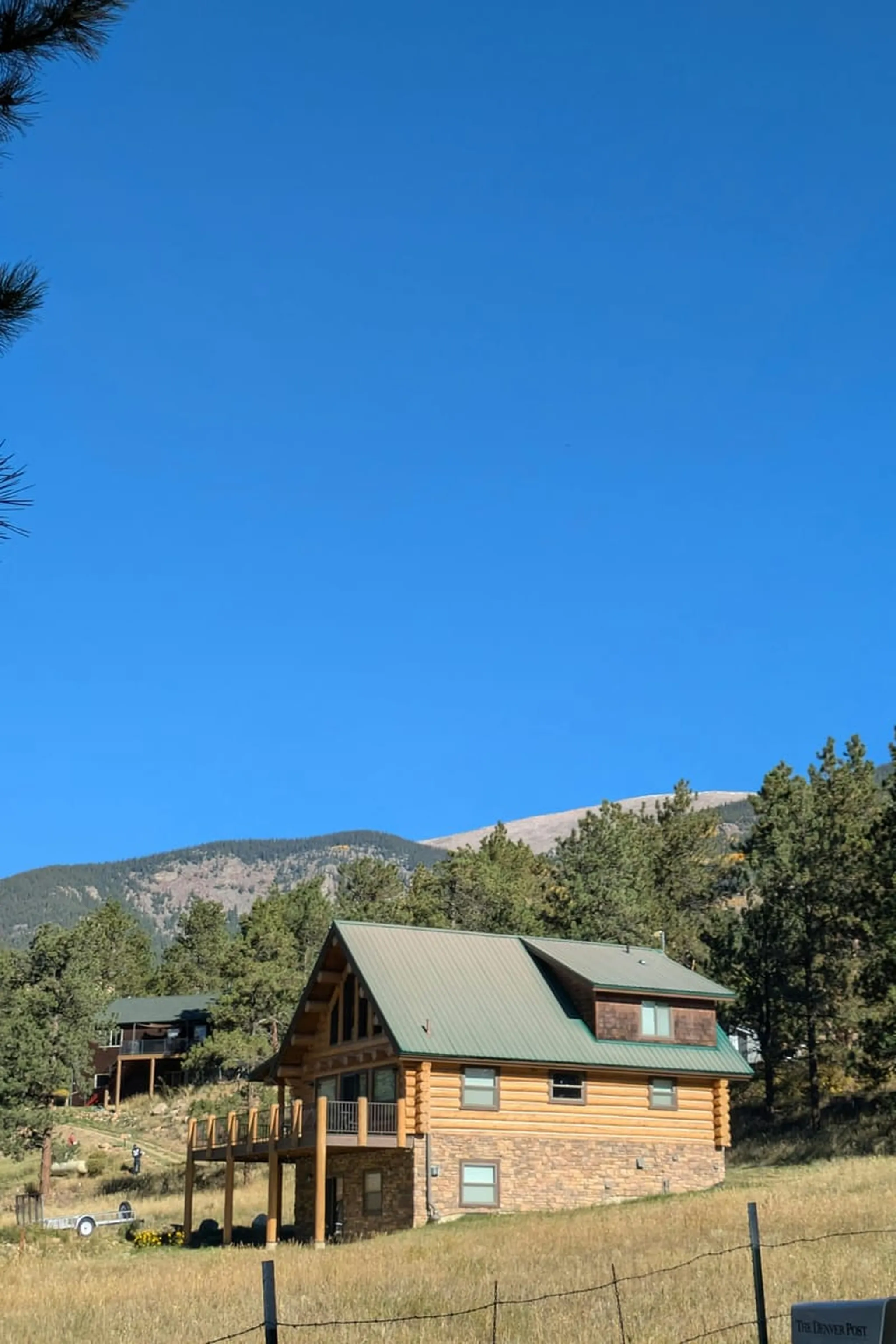 Rustic log cabin surrounded by lush forests and mountains under clear blue sky.