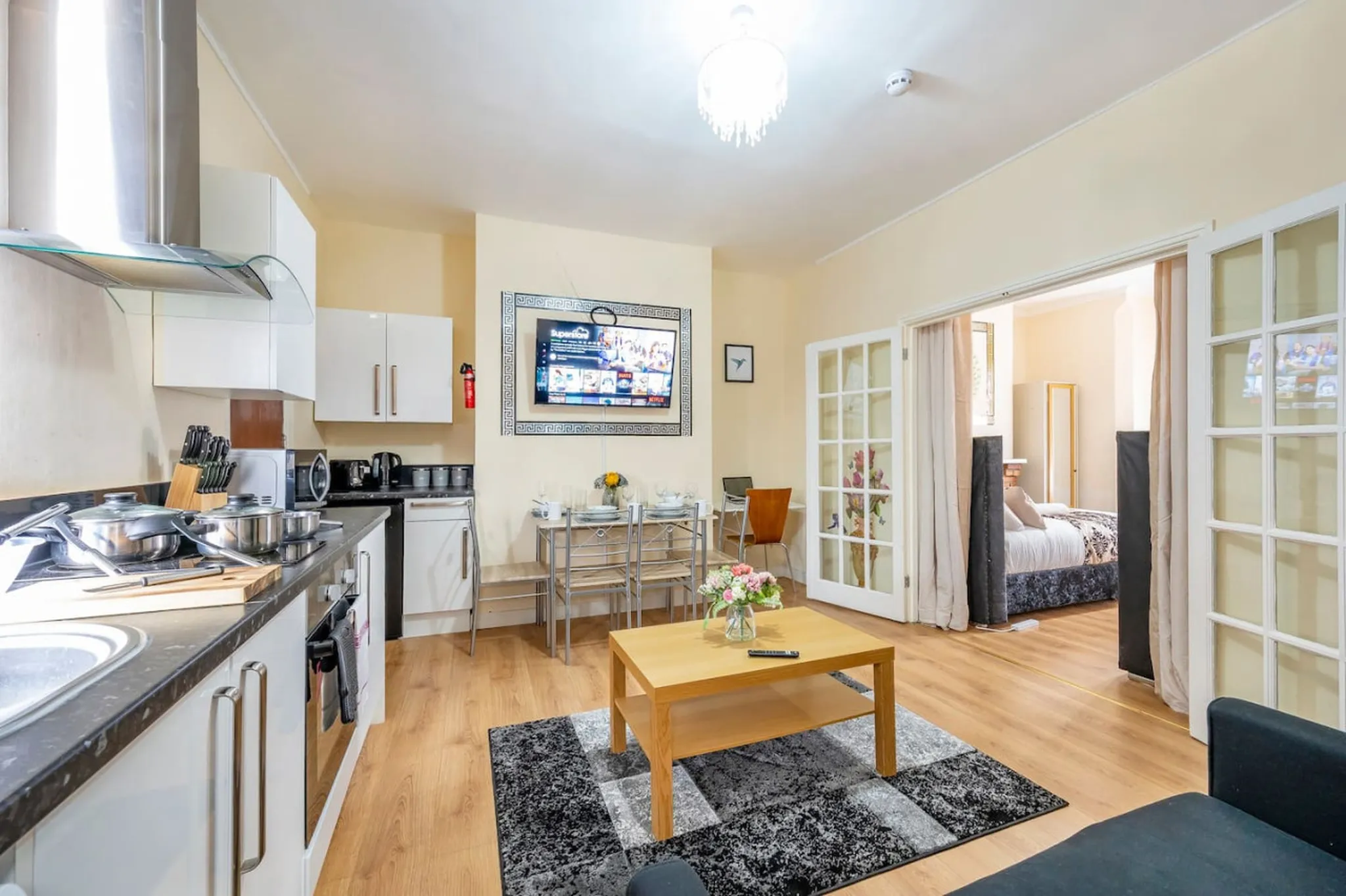 A modern apartment with a kitchen, dining area, and bedroom visible through glass doors.