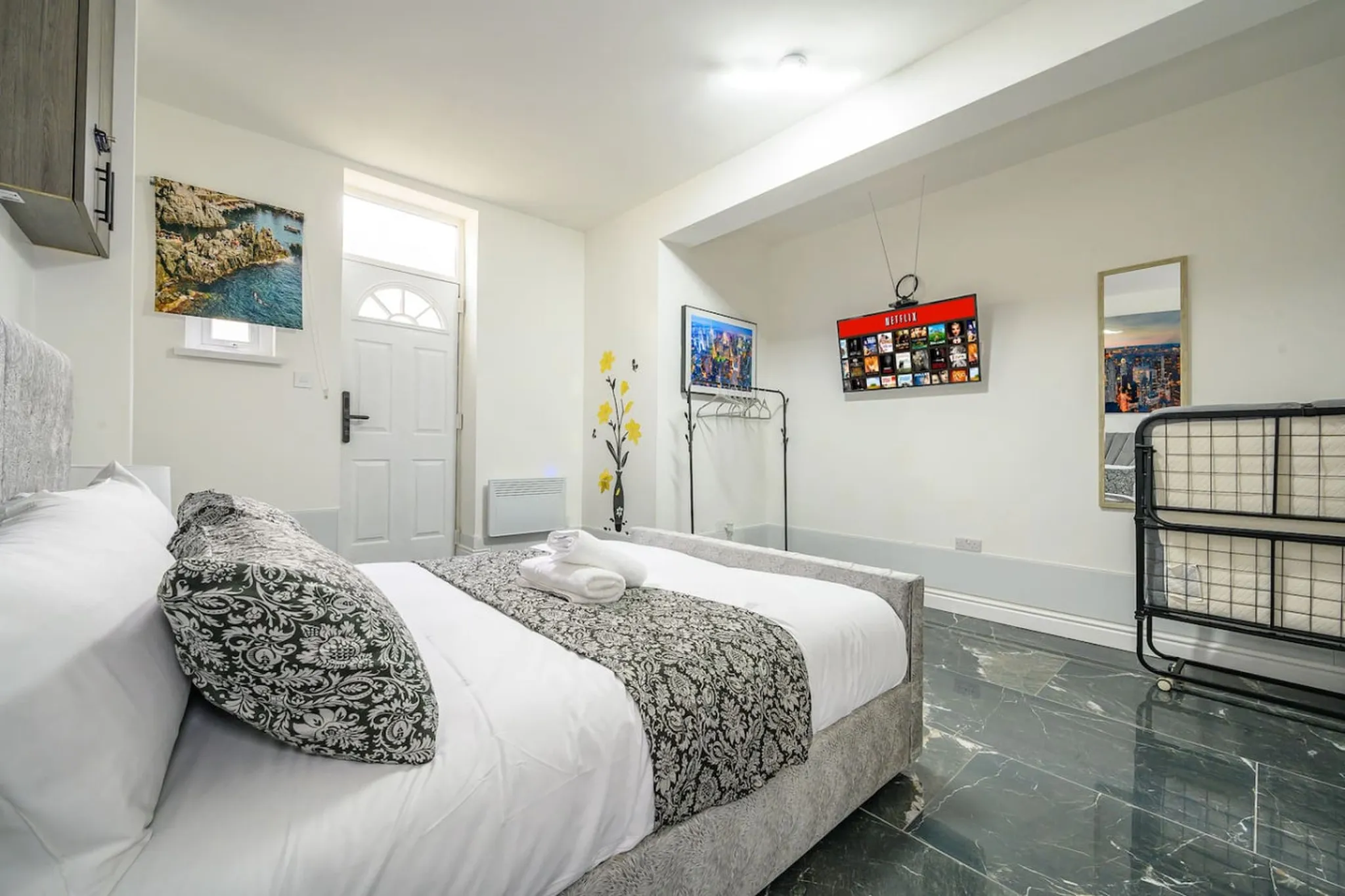 Bedroom with a queen bed, a TV showing Netflix, and a door with a window.