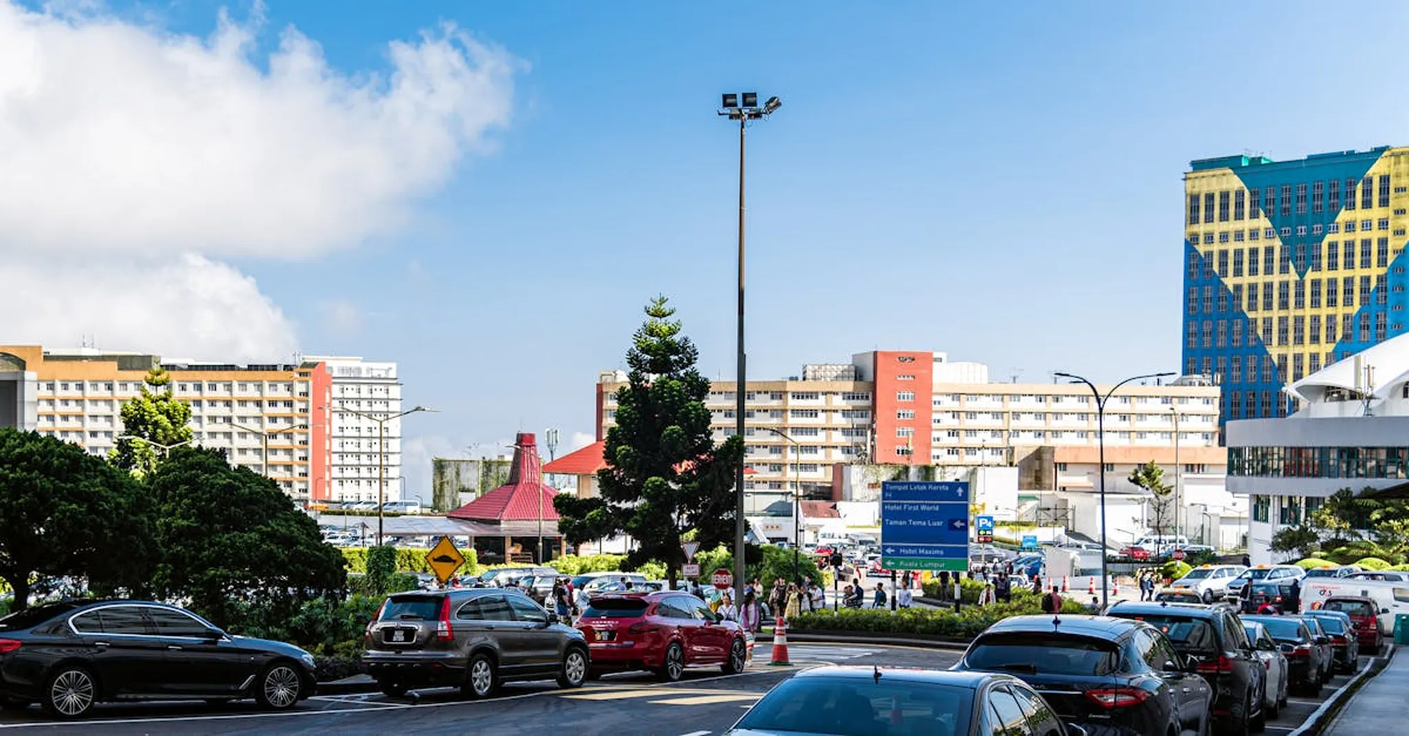 Urban scene in Genting Highlands with parked cars and city buildings under a bright sky.